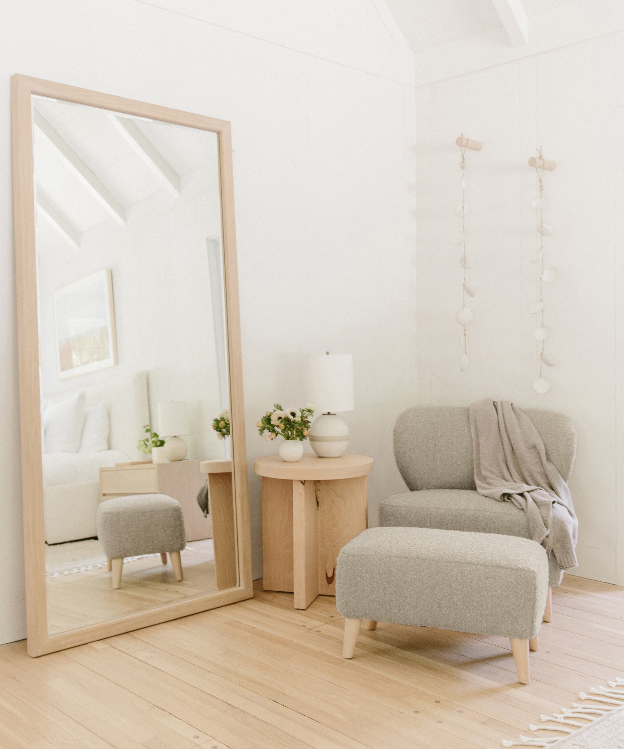 Jenni Kayne brentwood boucle chair and ottoman in a bedroom next to the marin side table and wall mirror with a throw on top.