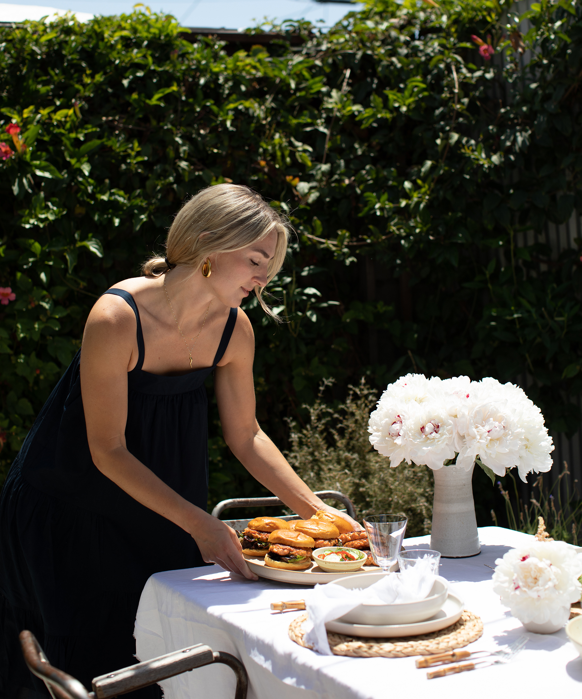 Olivia Muniak in her backyard placing a platter of salmon burgers on a table with flowers and a white table cloth.