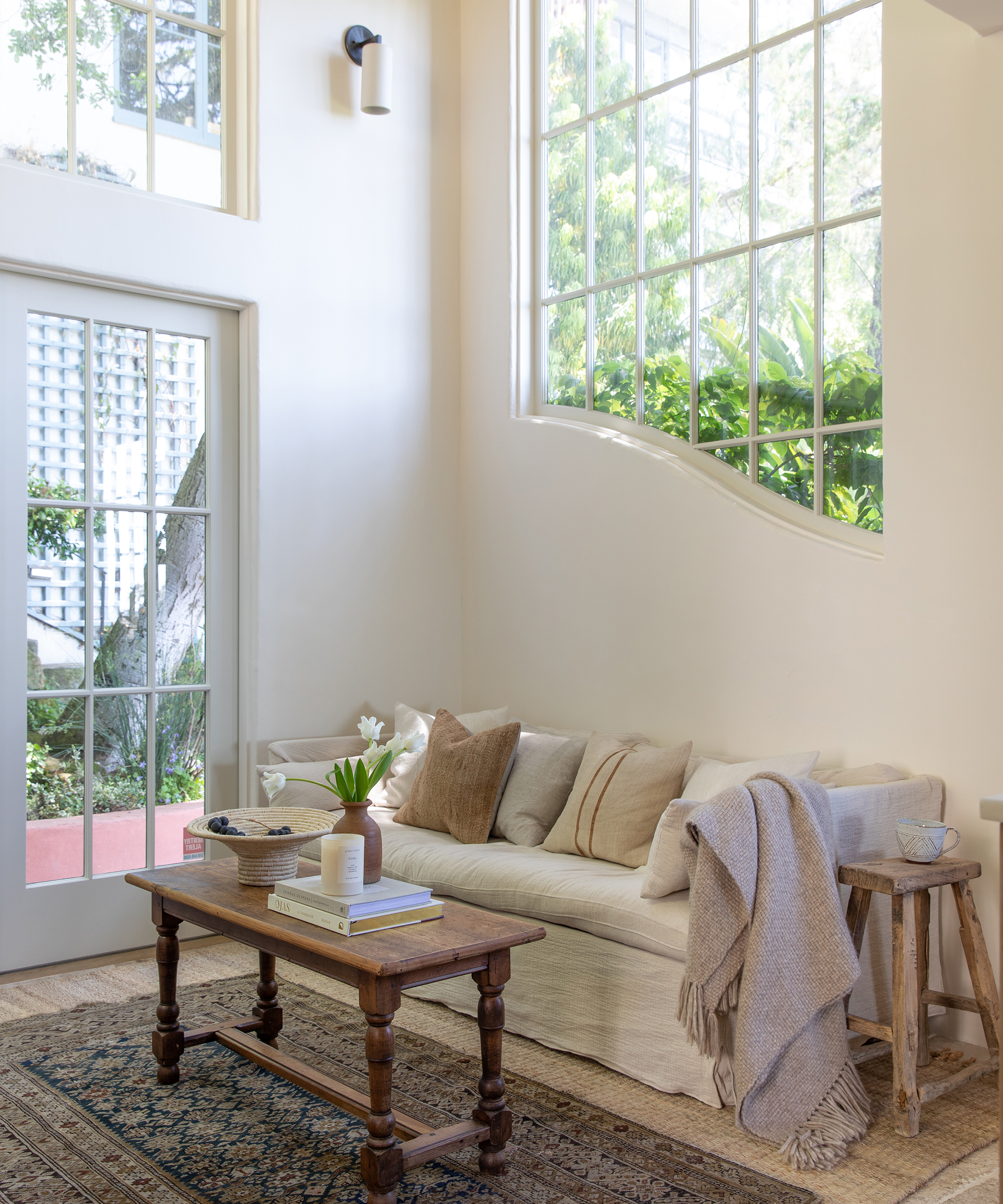 Image of Brodie Jenkins' living room with a linen sofa, pillows and throws on top, and a vintage coffee table and rug beside it.