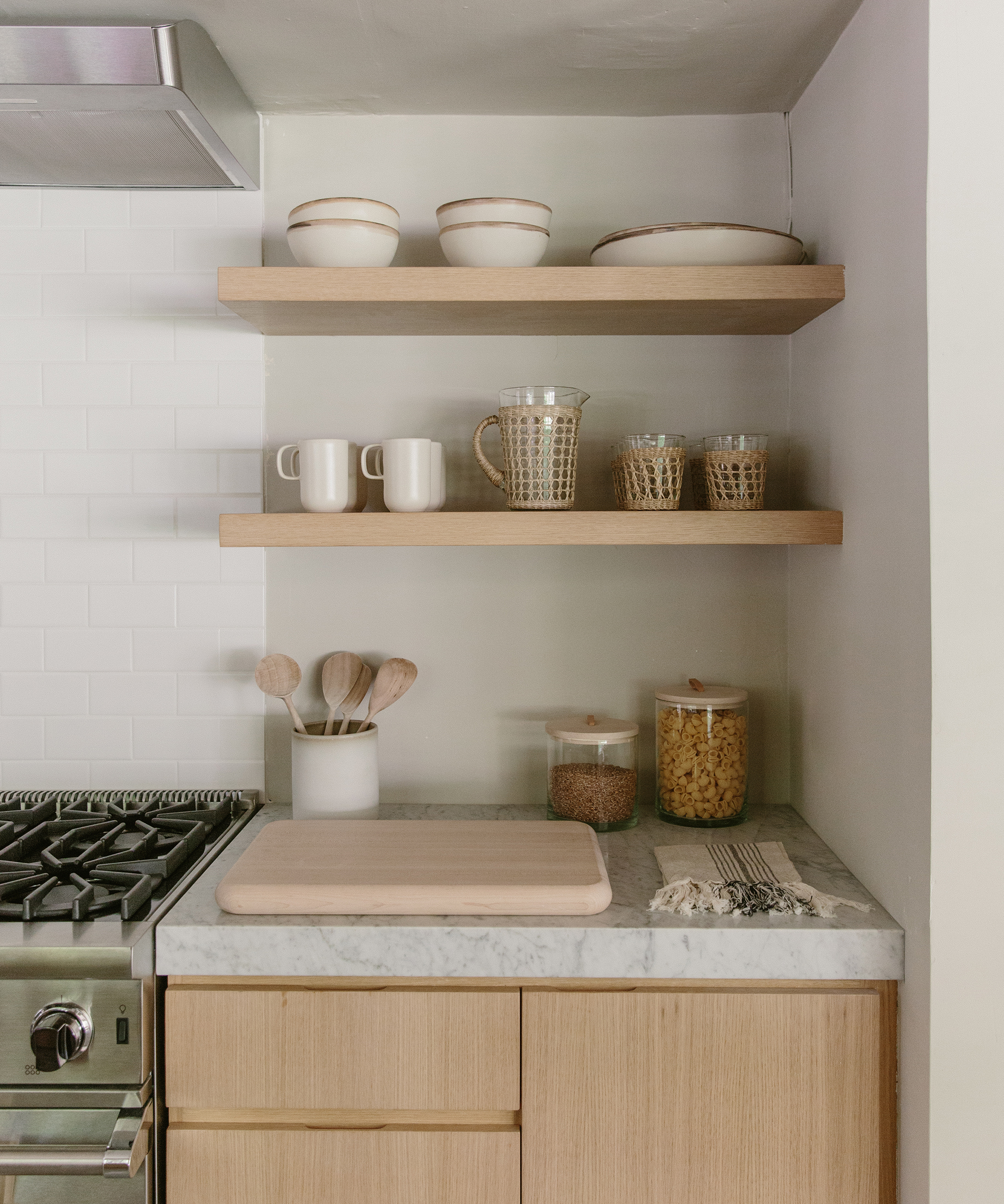 Julia Hunter's kitchen counter with oak wood shelving, marble countertops, and jenni kayne maple cutting board.