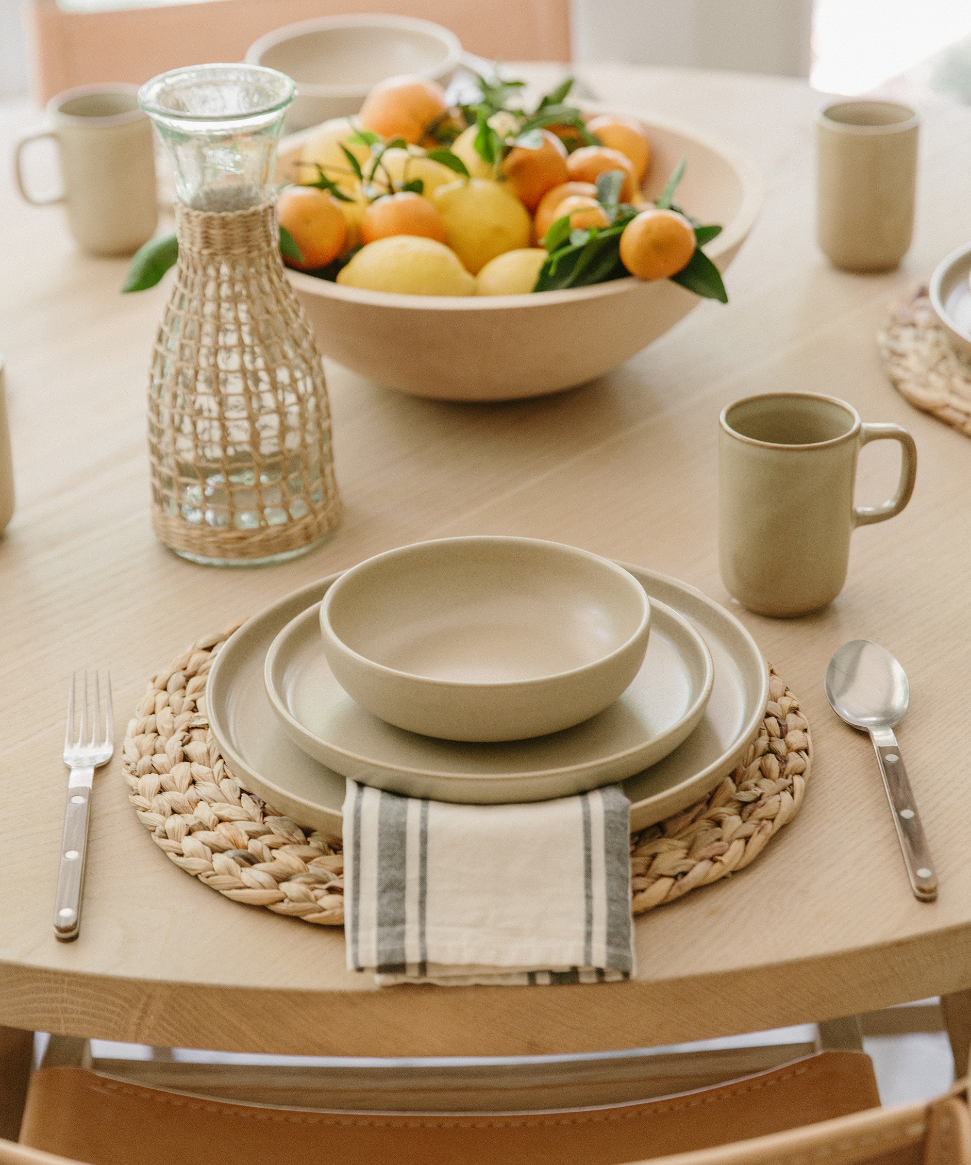 Close up shot of Julia Hunter's kitchen table with jenni kayne pacific dinnerware, woven charger, and a maple bowl with fruit inside.
