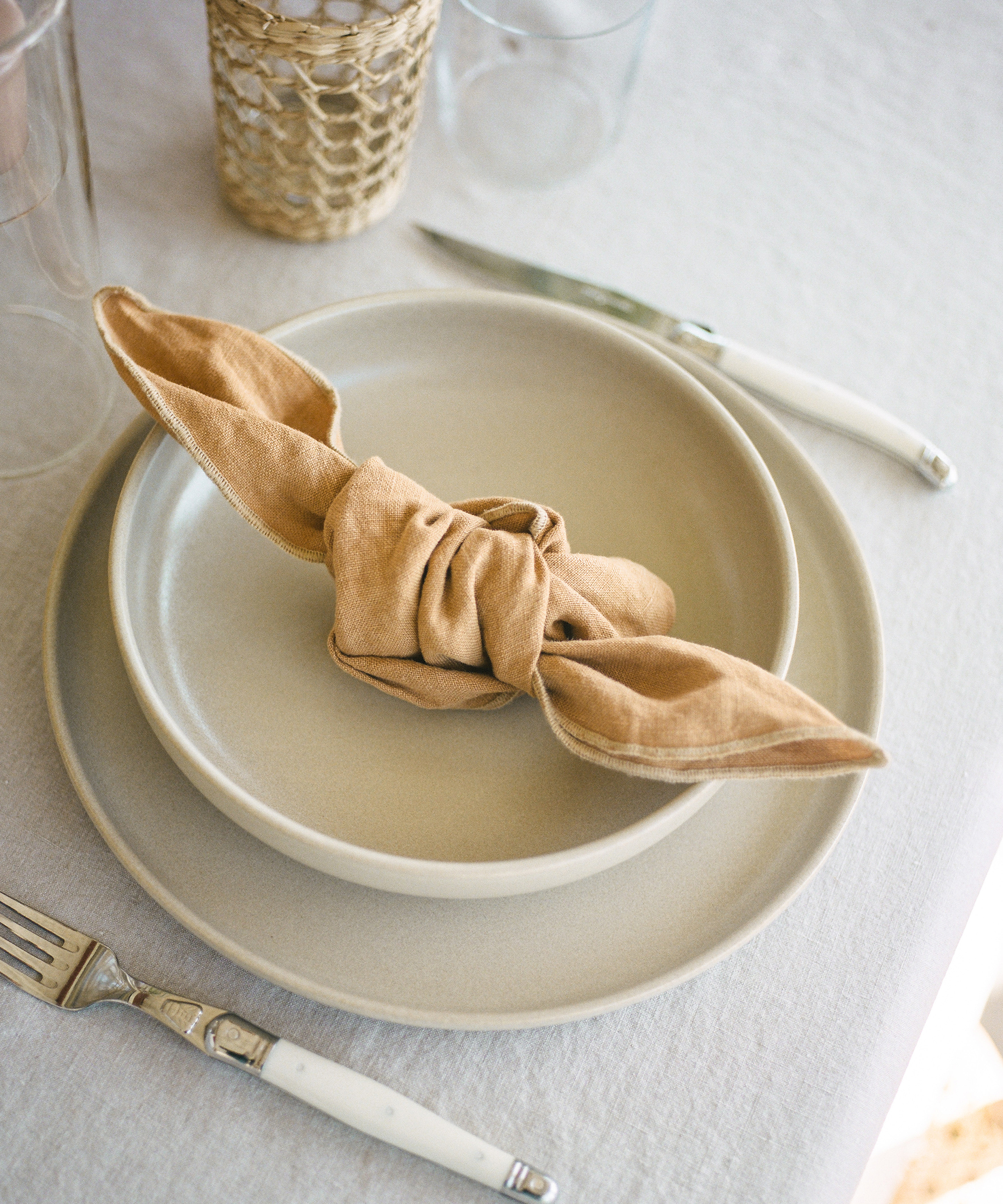 Pacific Dinnerware on top of a white linen tablecloth with rattan cups and plants on the table.
