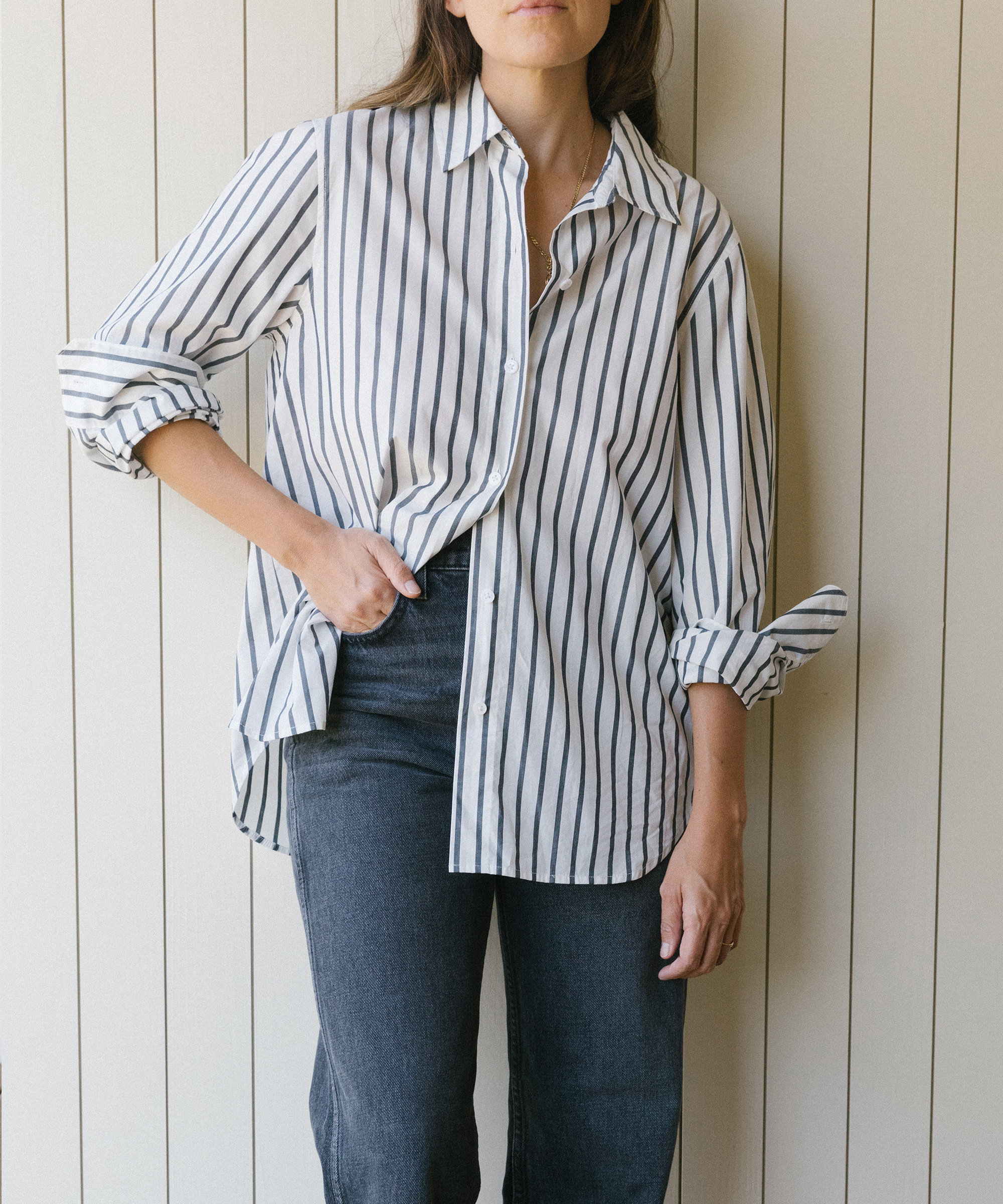 Kate Brien standing against a white wall wearing striped classic shirt and jeans.