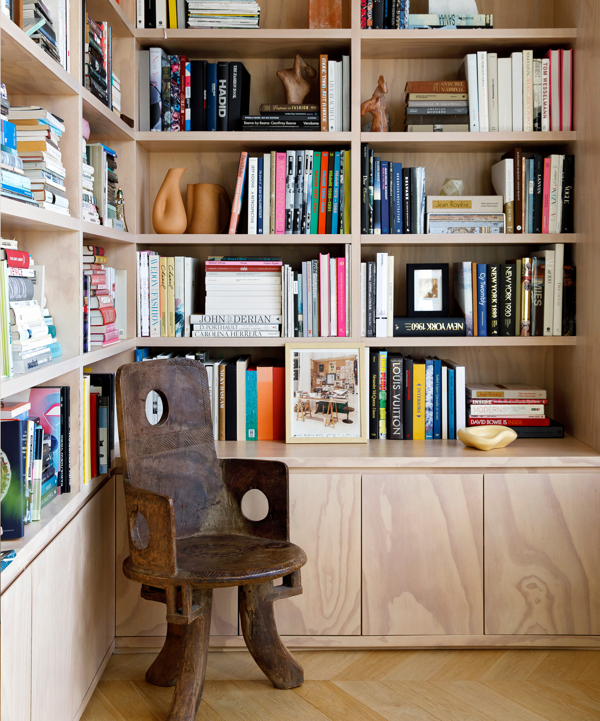 A cozy reading nook with built-in wooden bookshelves, inspired by Jane Keltner de Valle’s elegant style, filled with colorful books, decorative objects, and art pieces. In front, a rustic wooden chair with a distinctive design invites relaxation.