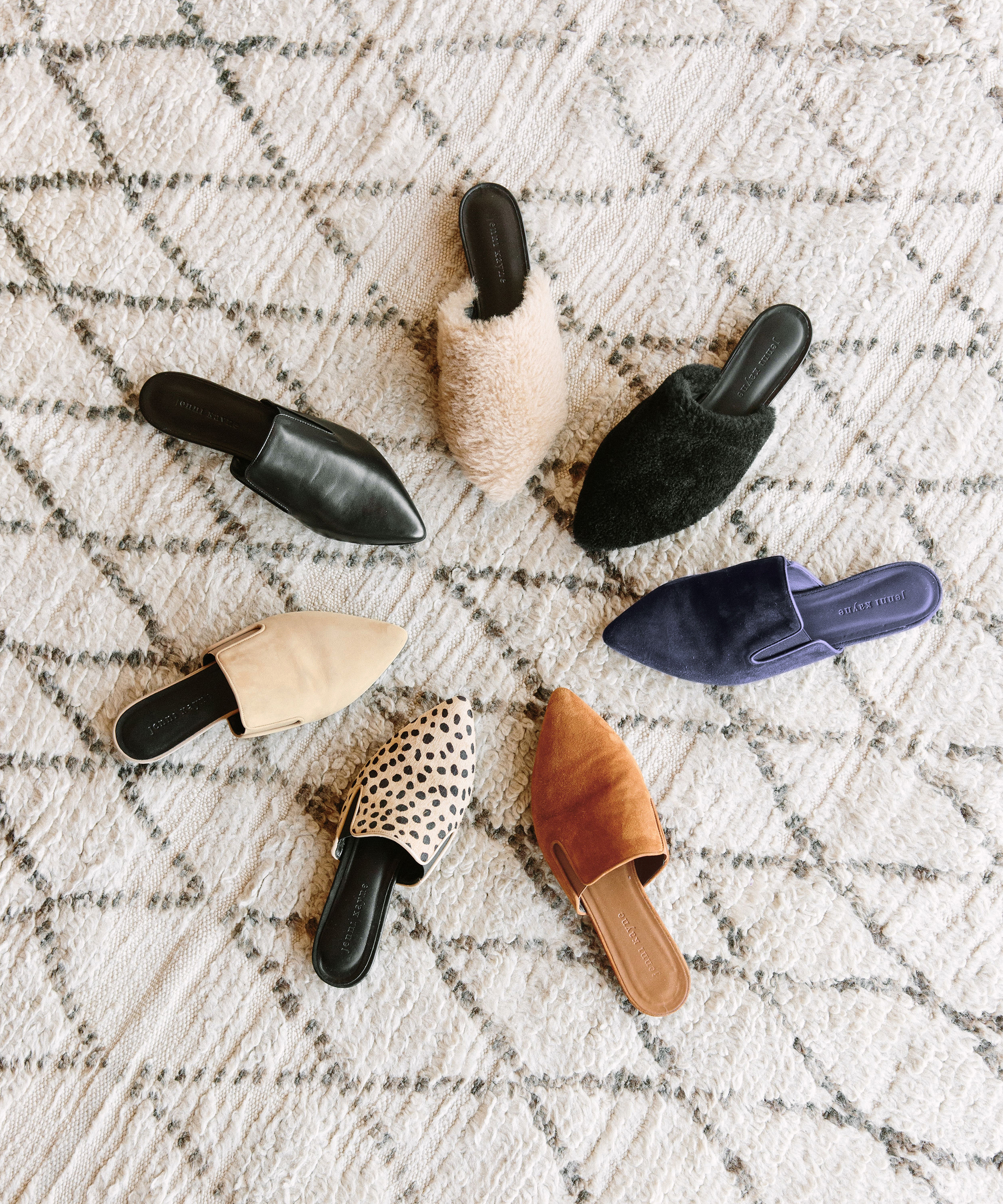 Jenni Kayne Mules in various colors sitting in a circle with toe pointed inwards on top of a patterned rug.