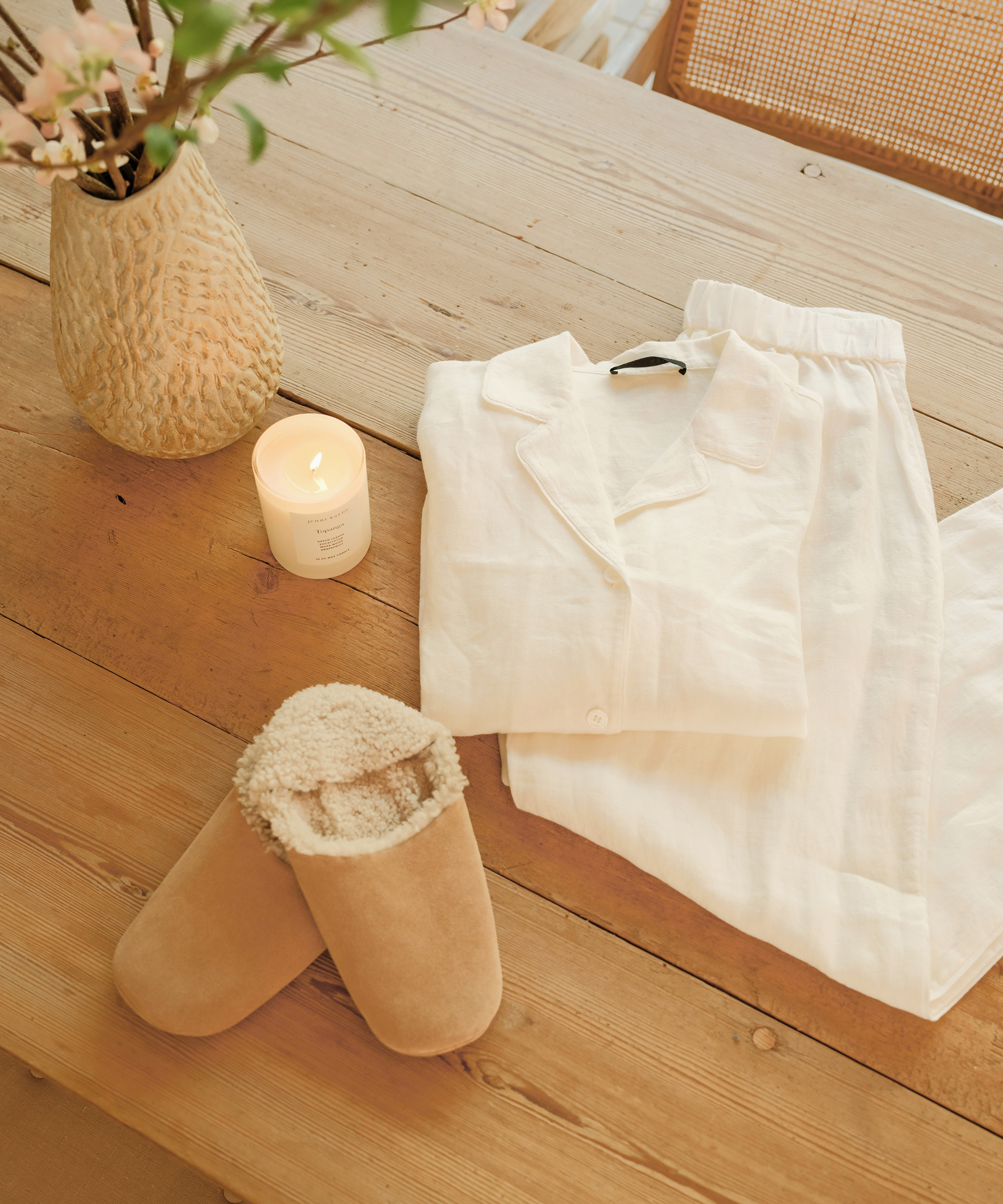 oak table with folded ivory pajamas suede slippers and burning topanga candle