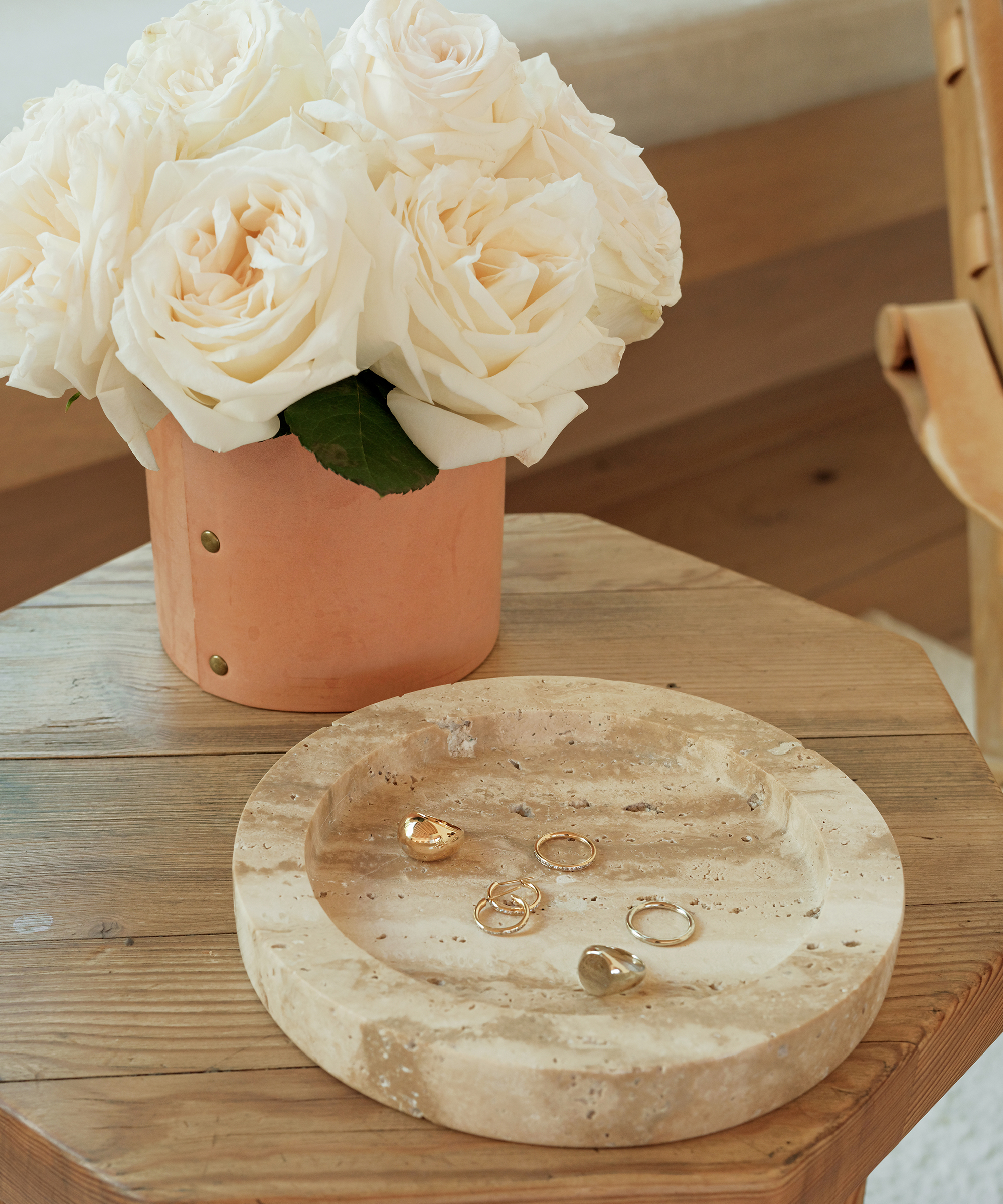 A beige stone tray with several gold and silver rings sits on a wooden table next to a terracotta pot filled with large white roses—stylish inspiration for valentines day gift ideas for him.
