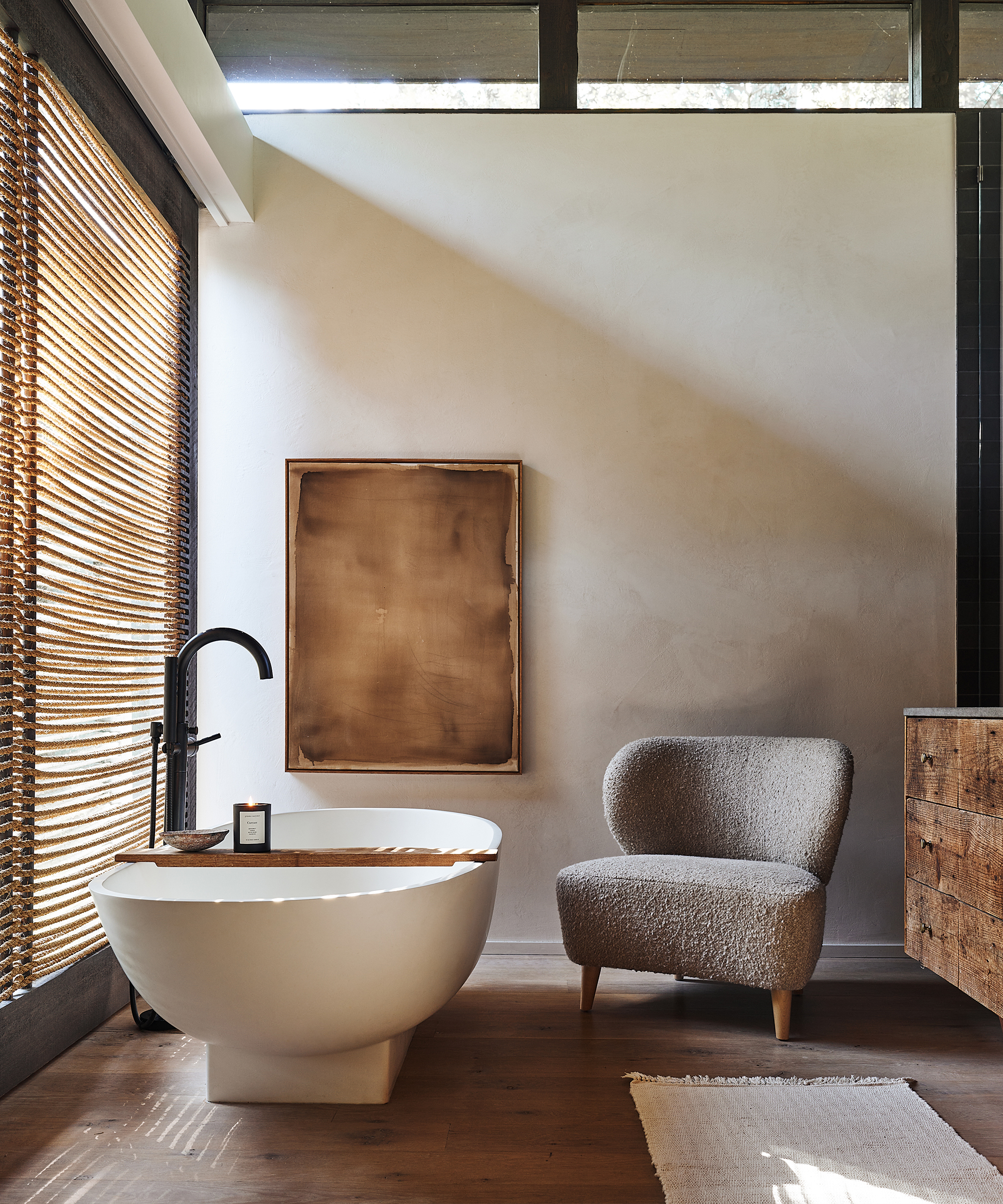 grey boucle accent chair next to a standalone bathtub in a bathroom