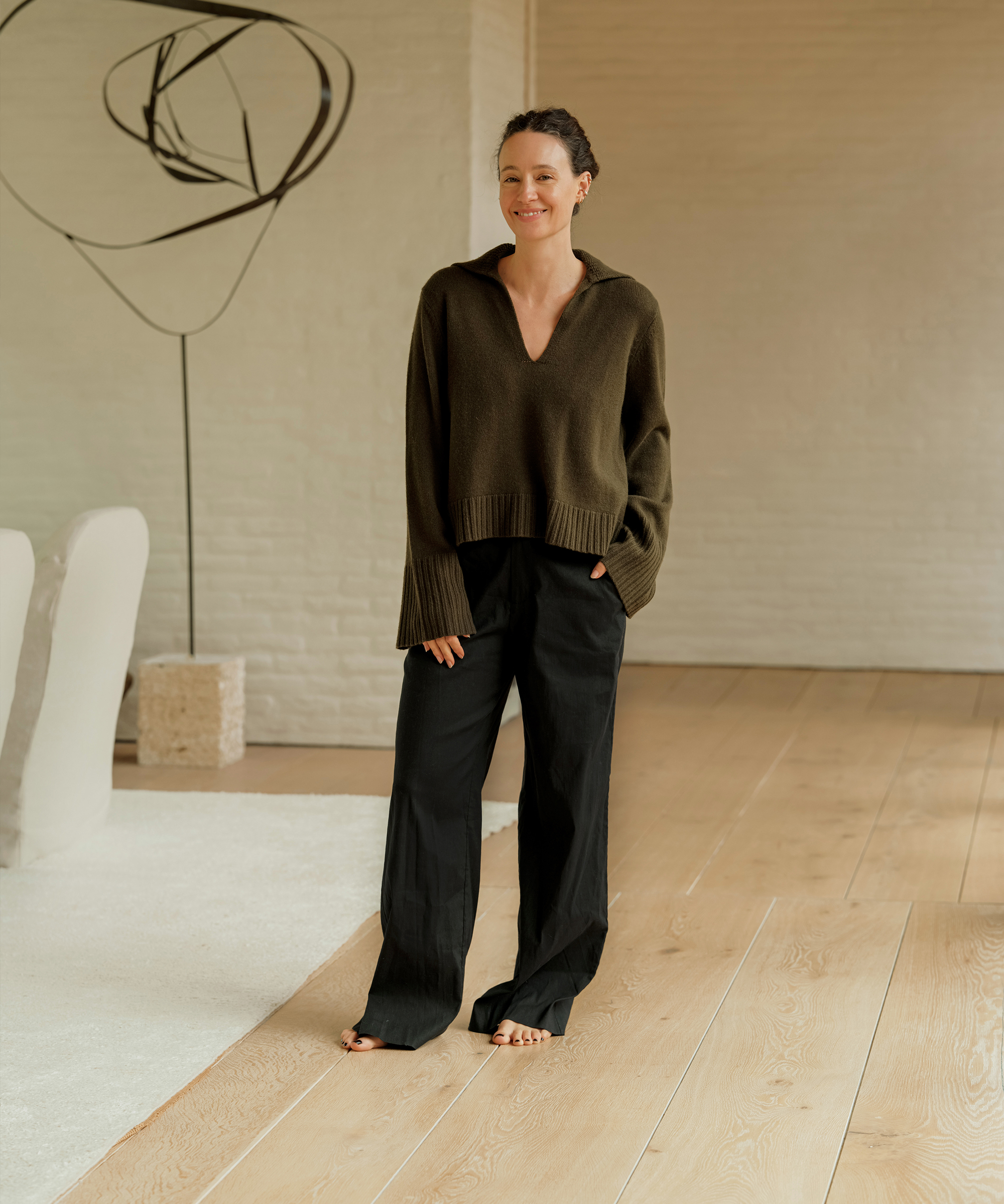 jenni kayne standing in her living room in an olive green polo and black trousers