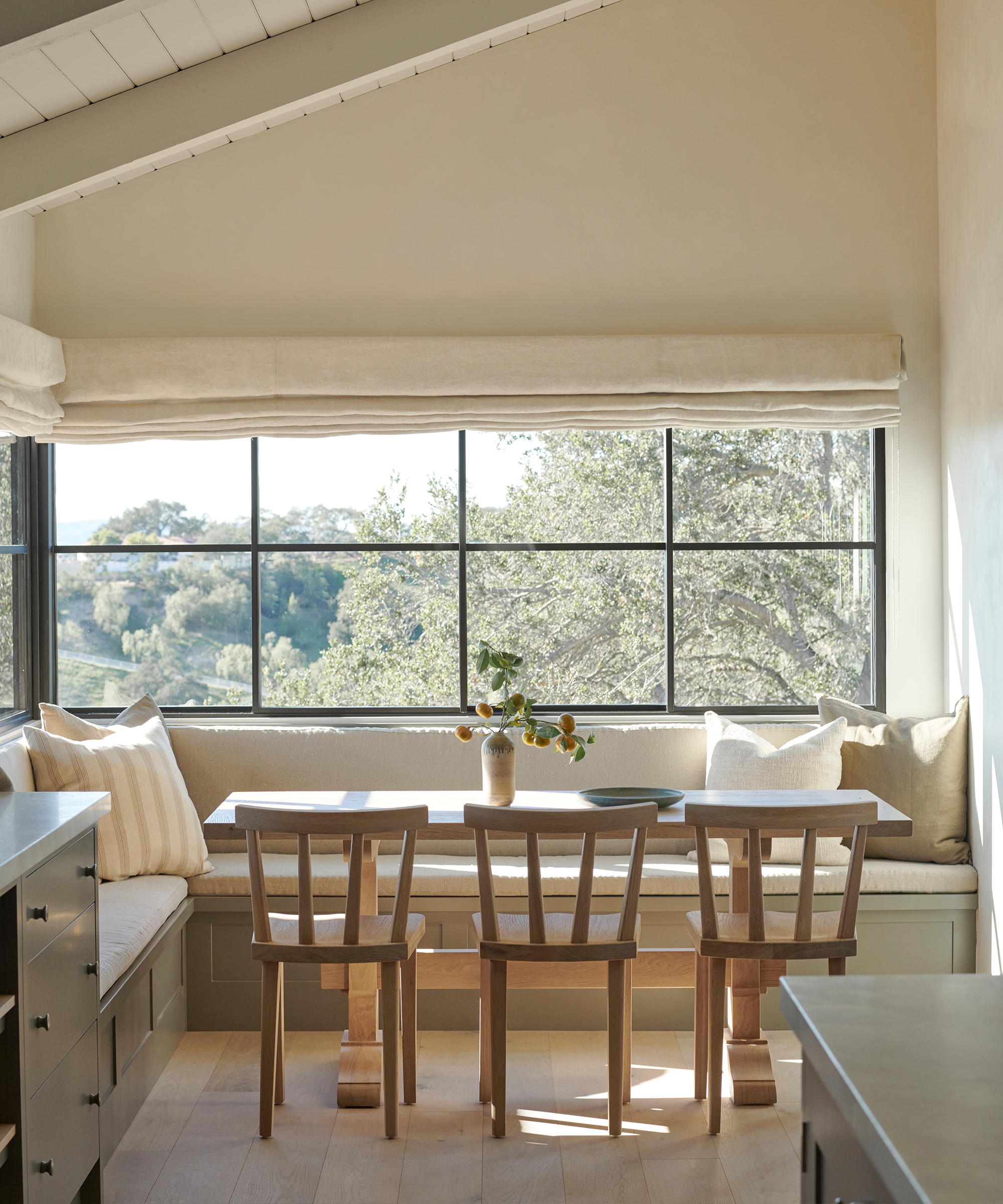 built in kitchen nook with three wooden chairs and sunlit windows with black window panes