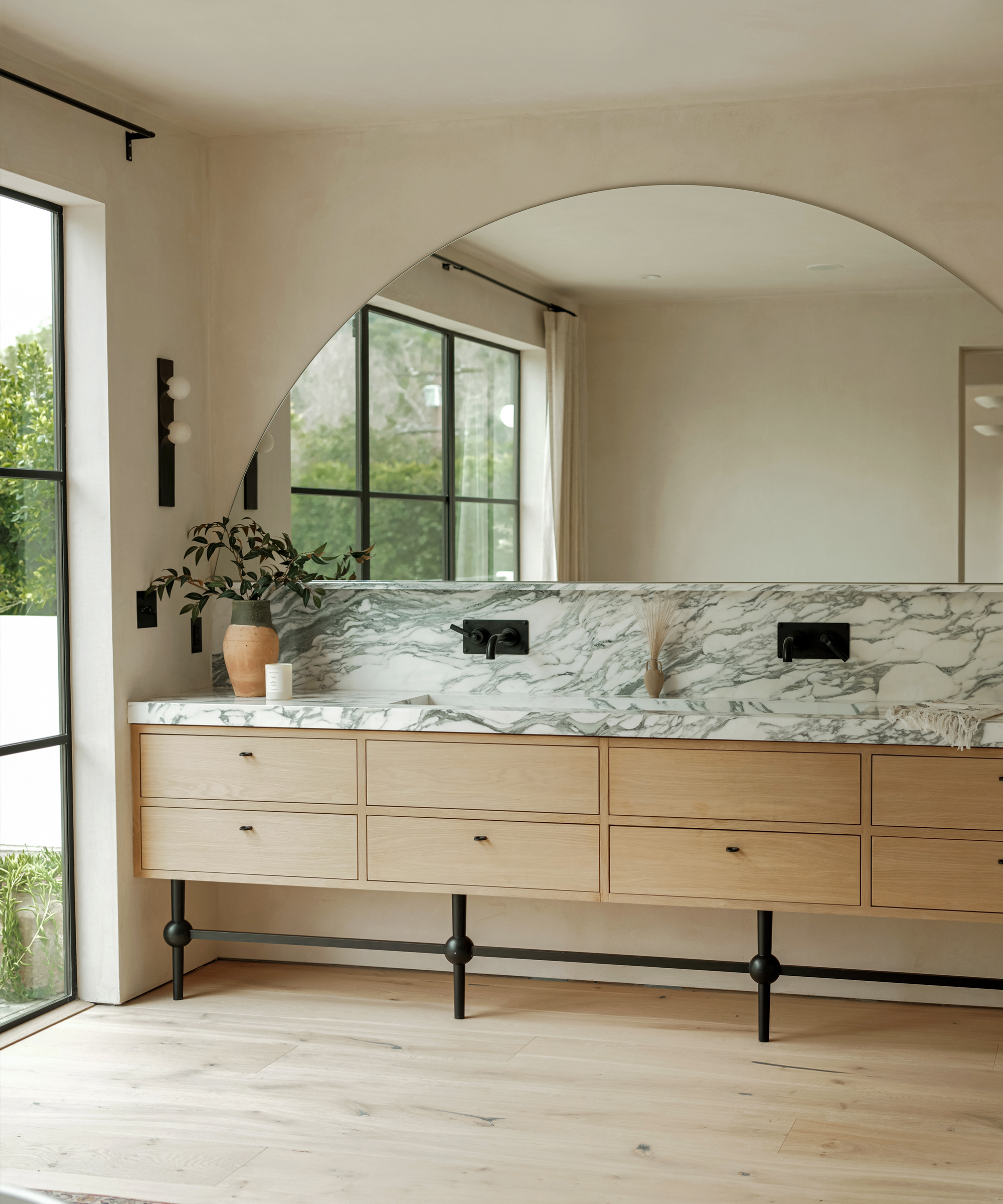 large primary bathroom vanity with a curved half oval mirror oak cabinetry and marble counters