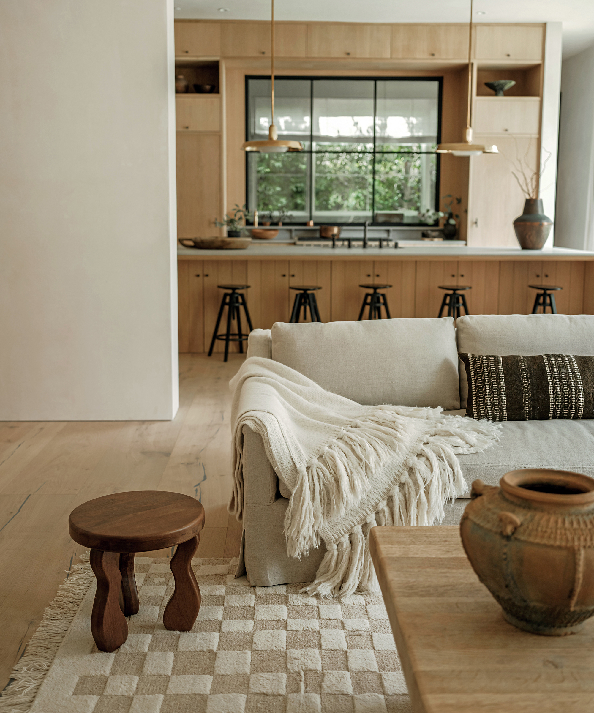 checkered rug and light grey couch with a wooden stool in front of open kitchen living room plan