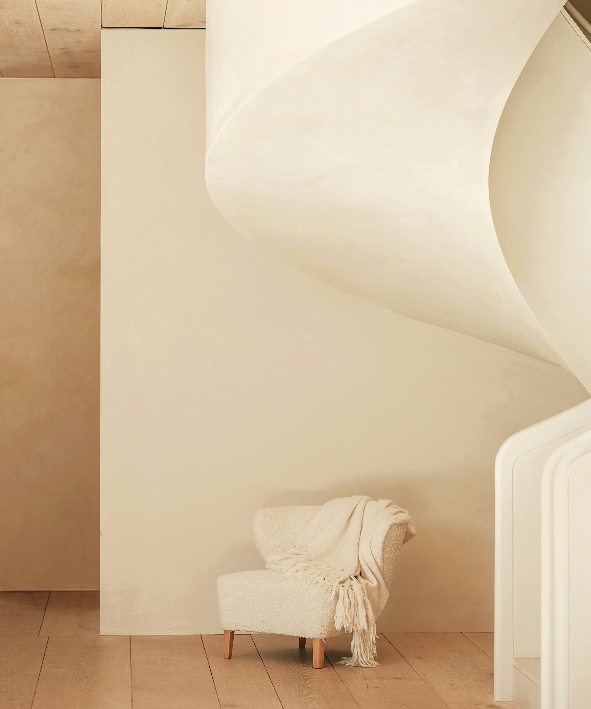 cream brentwood boucle chair with a mohair throw draped over it sitting under a white stairwell