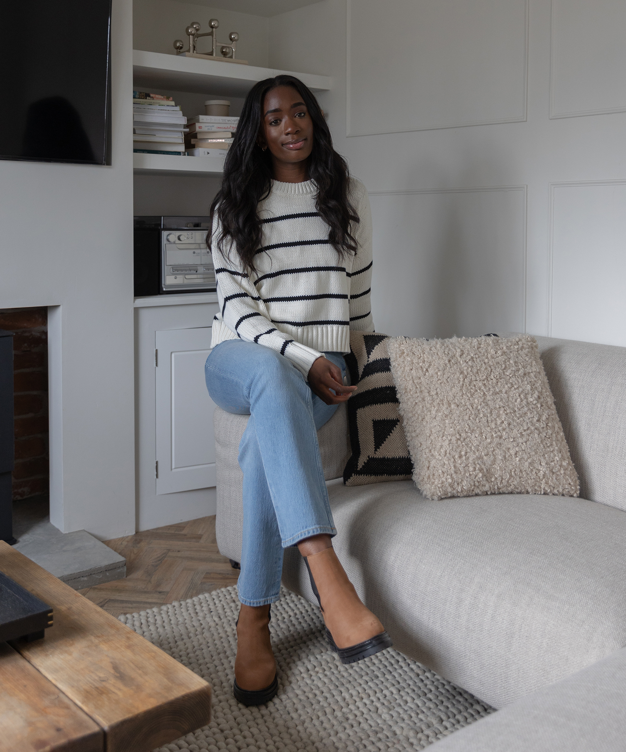 woman sitting on the couch in jeans and tan boots a white and black striped cotton sweater