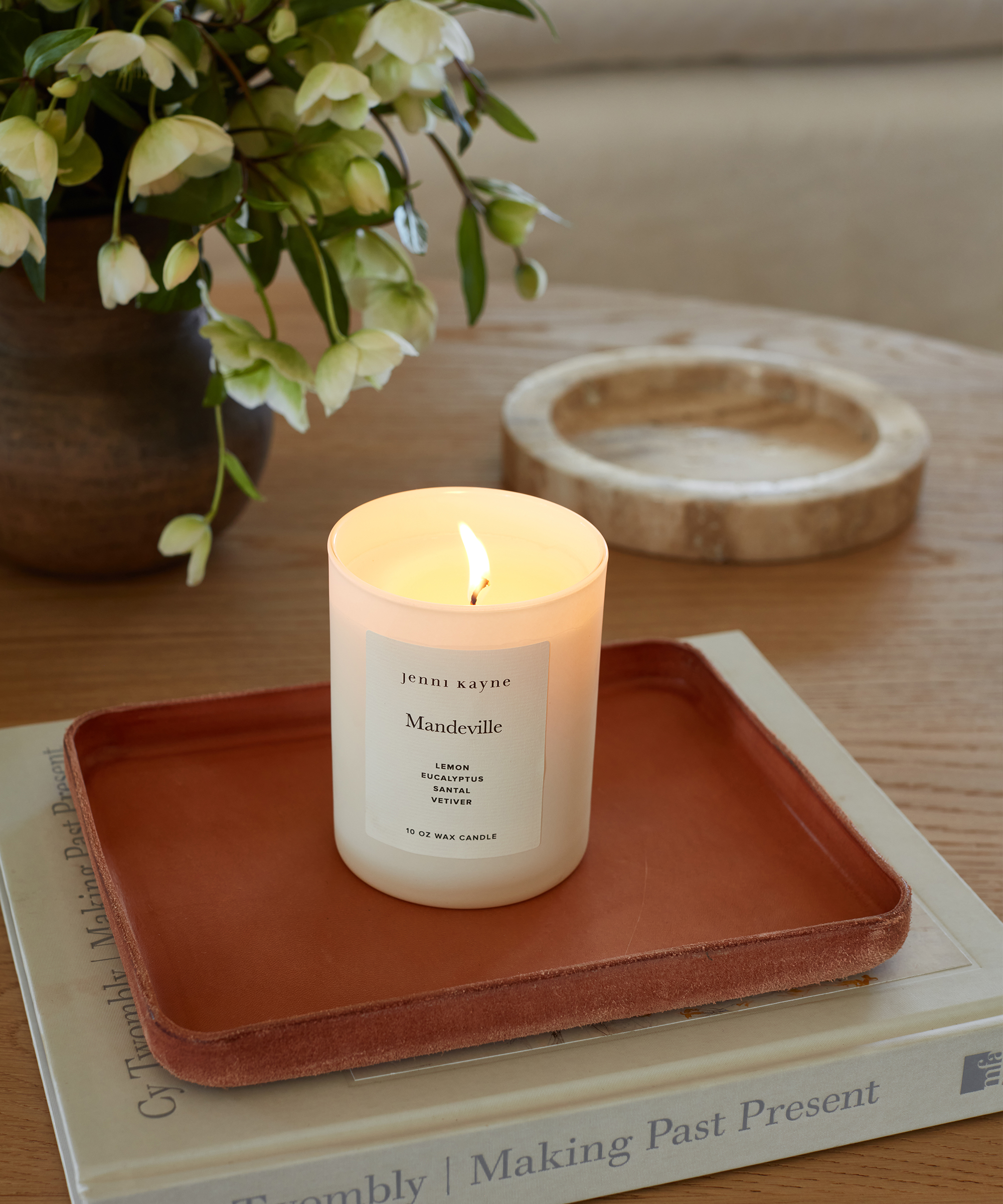 a jenni kayne candle burning on a coffee table with a leather catchall and coffee table books