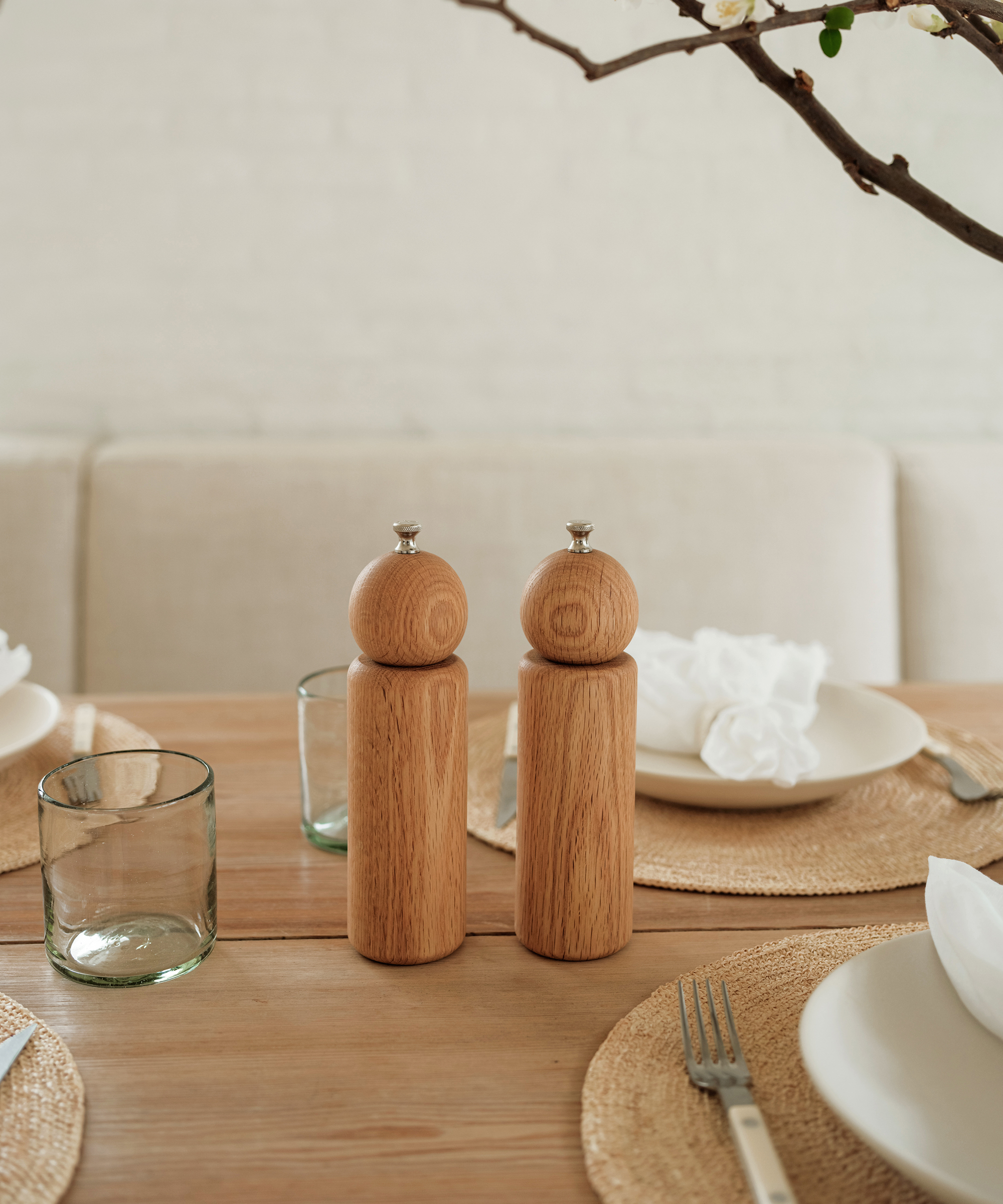 wooden salt and pepper shakers on an oak dining room table next to place settings with linen napkins