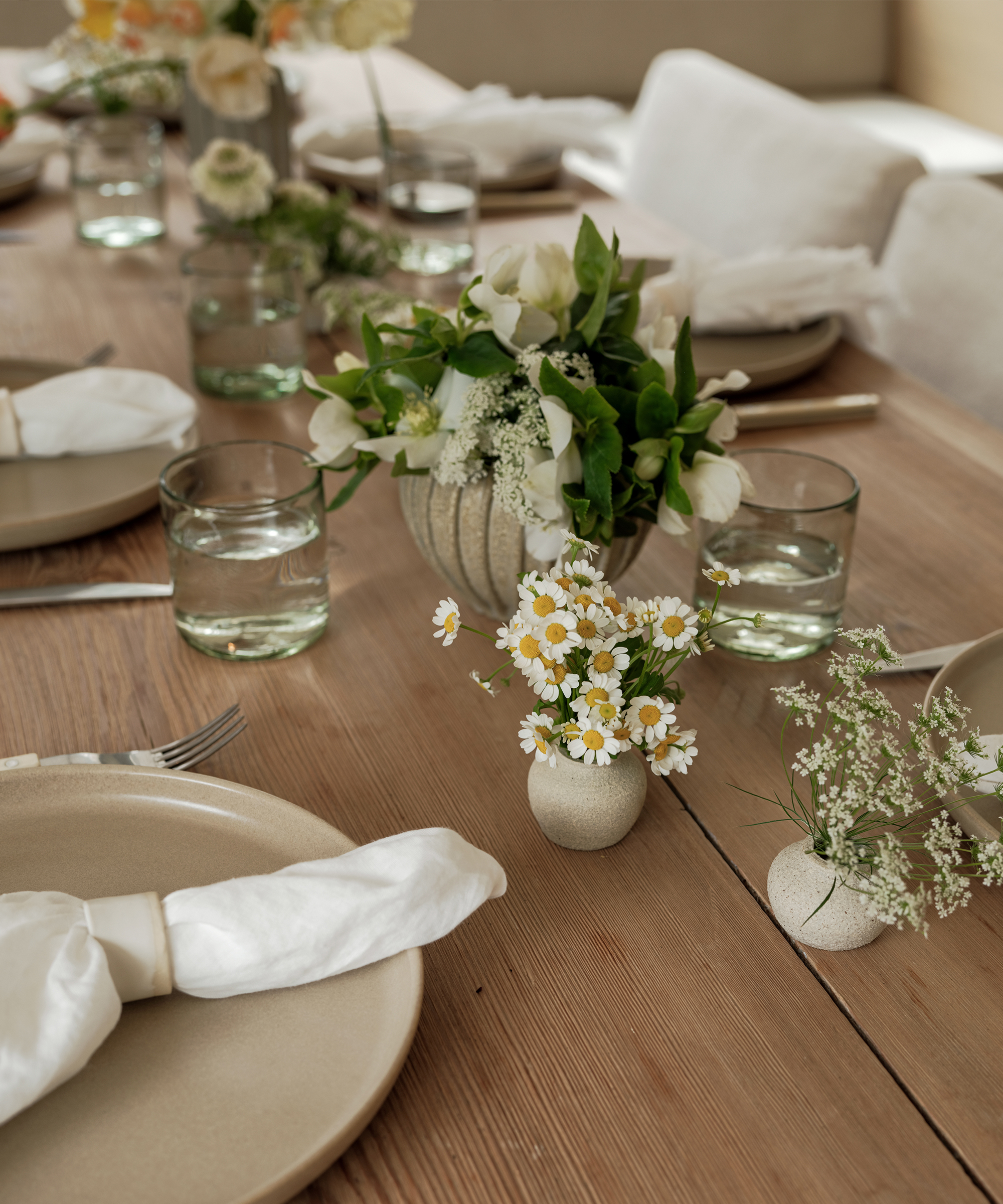white and yellow flowers in small ceramic cases on an oak dining table