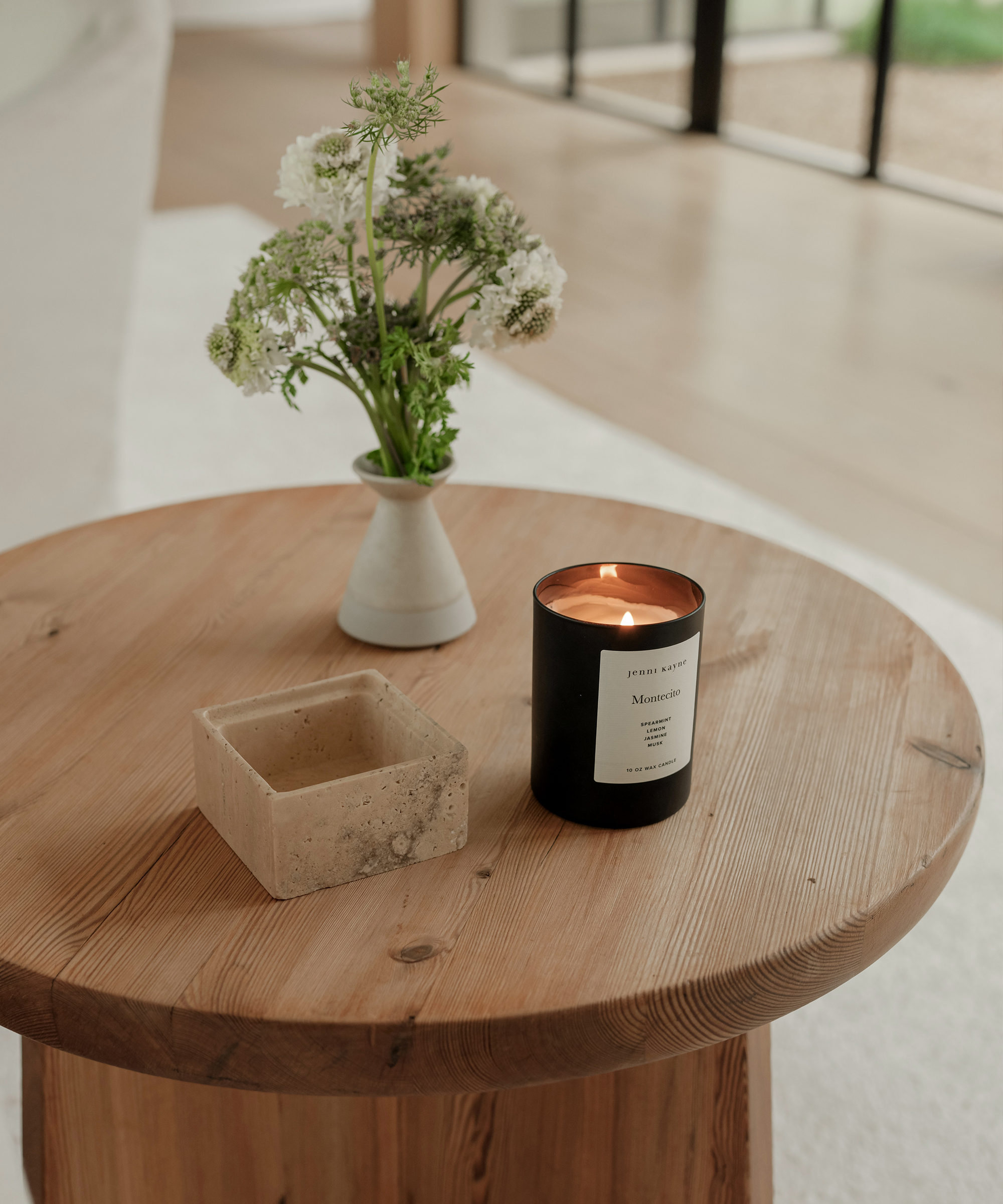 black candle burning on an oak side table with a green and white small floral arrangement