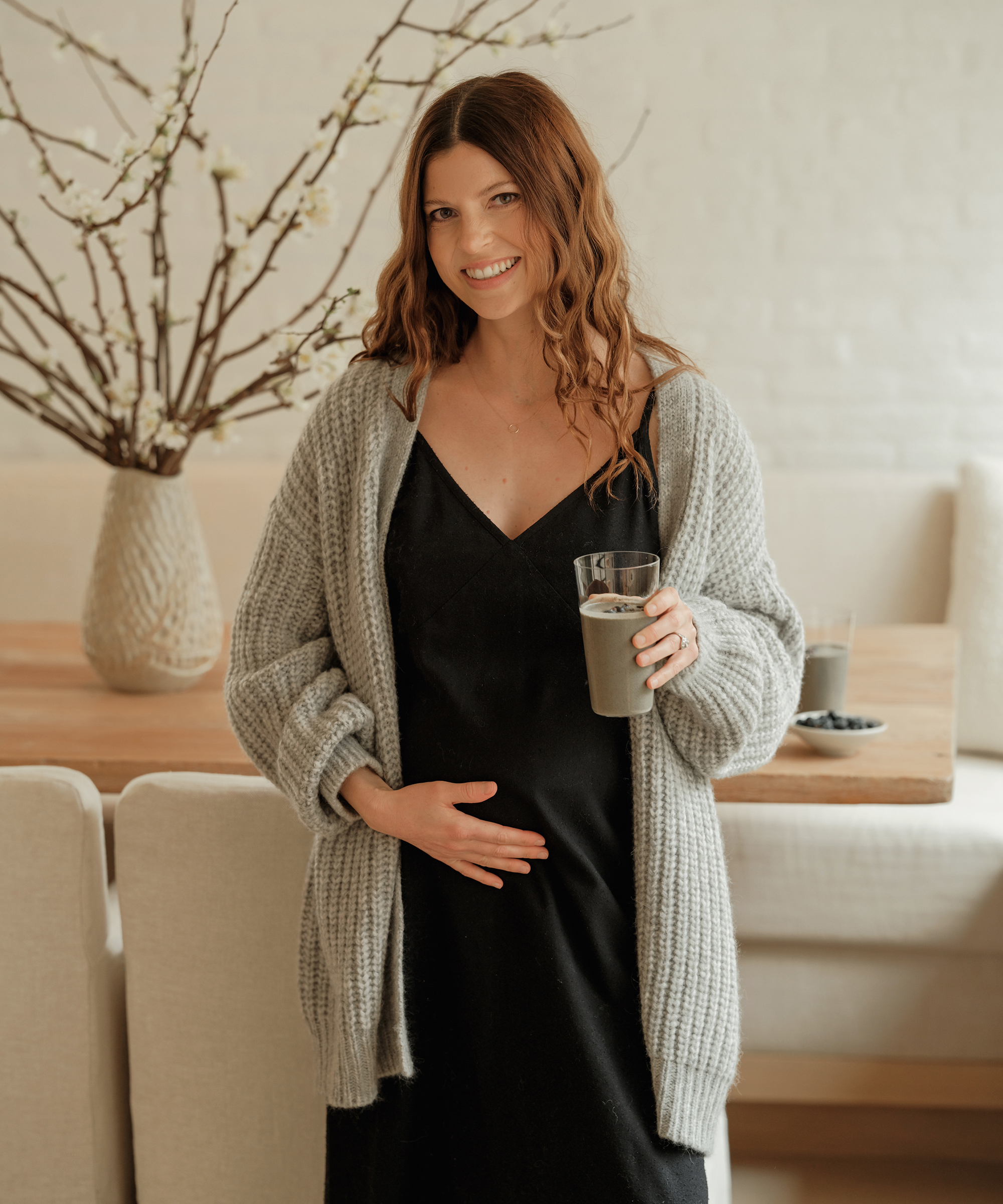 woman in a black maxi dress and grey cocoon cardigan holding a smoothie