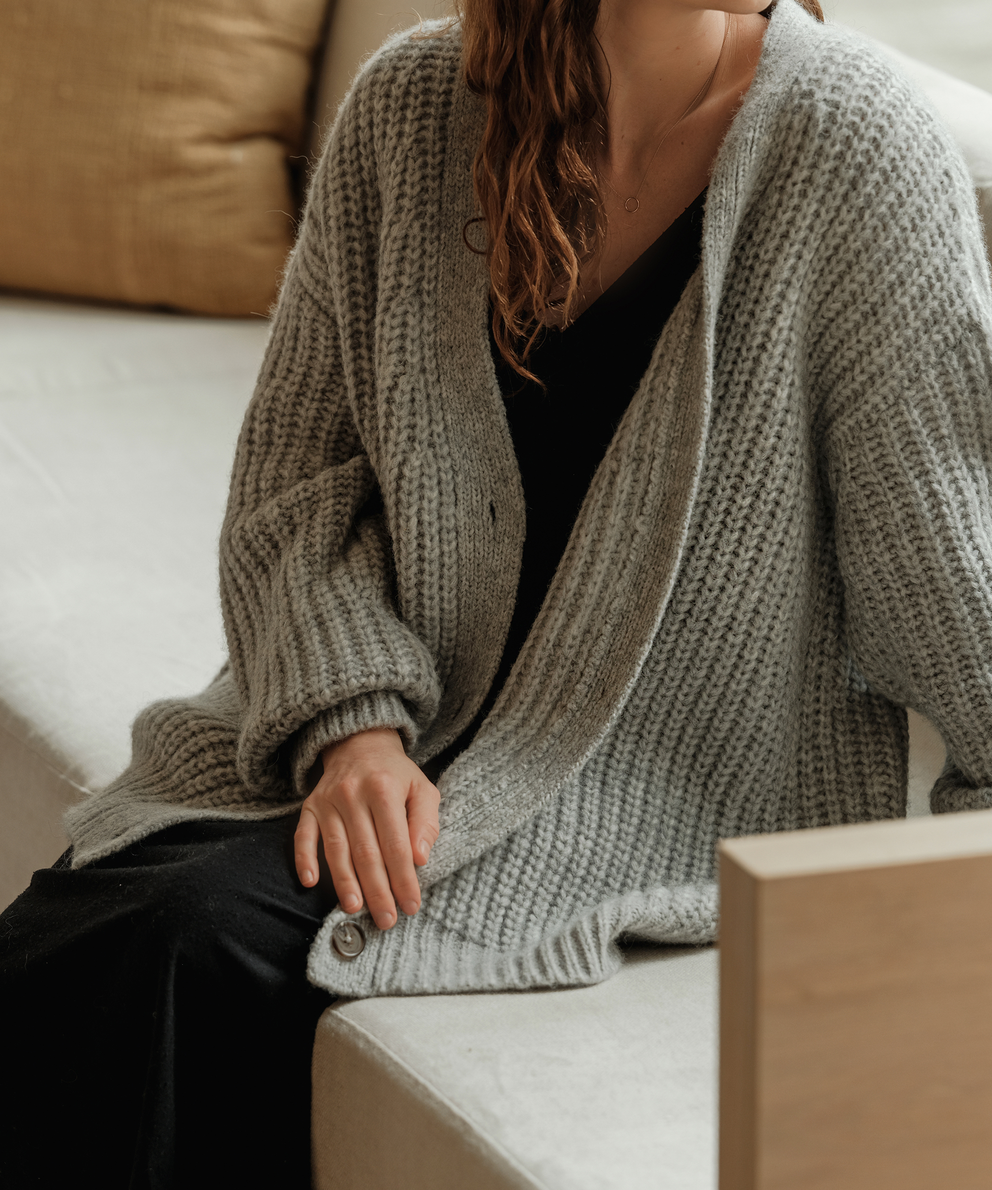 woman sitting on a built in couch in a black dress and grey cocoon cardigan