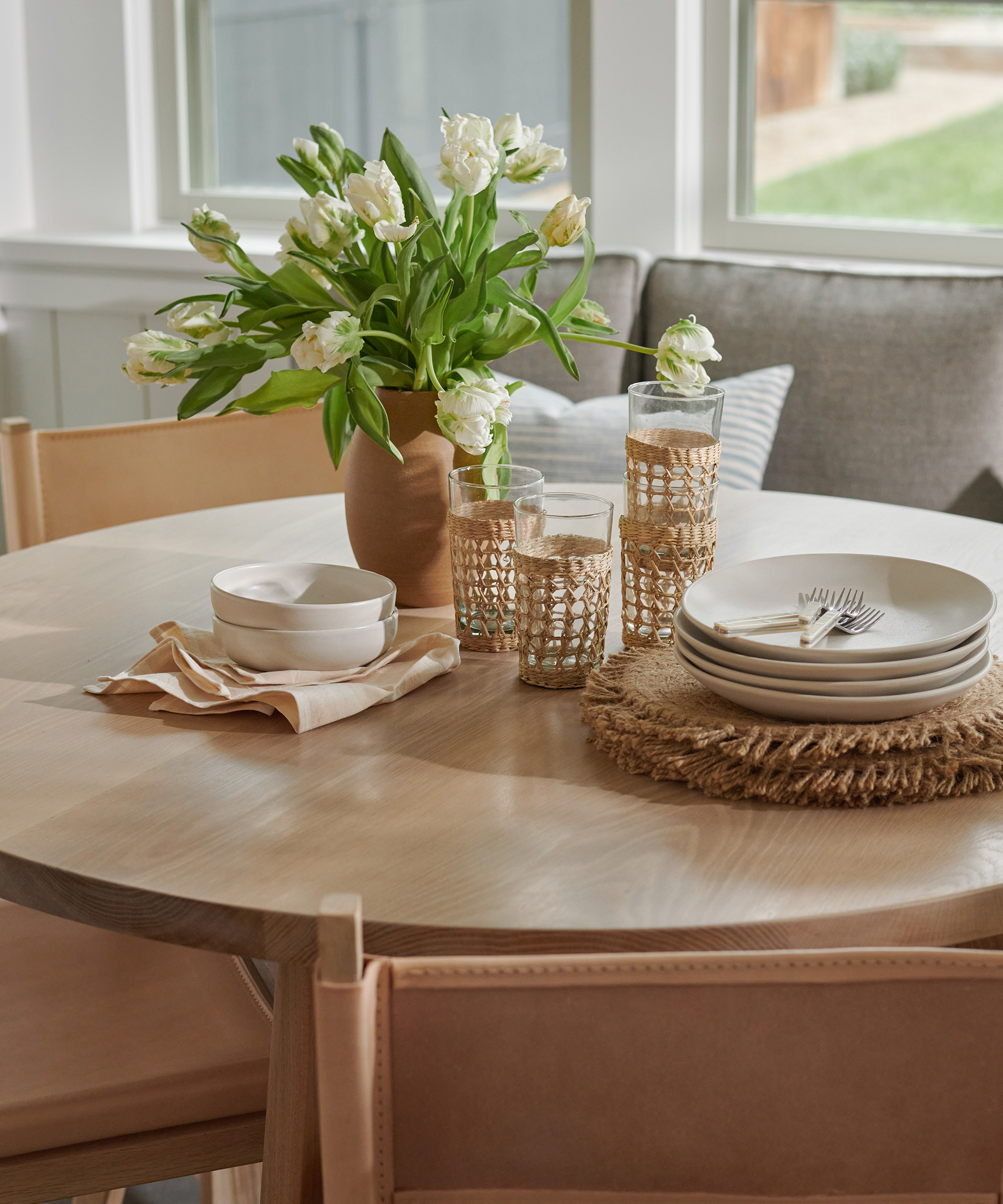 oak dining table with white tulips and rattan tumblers and ivory dinnerware