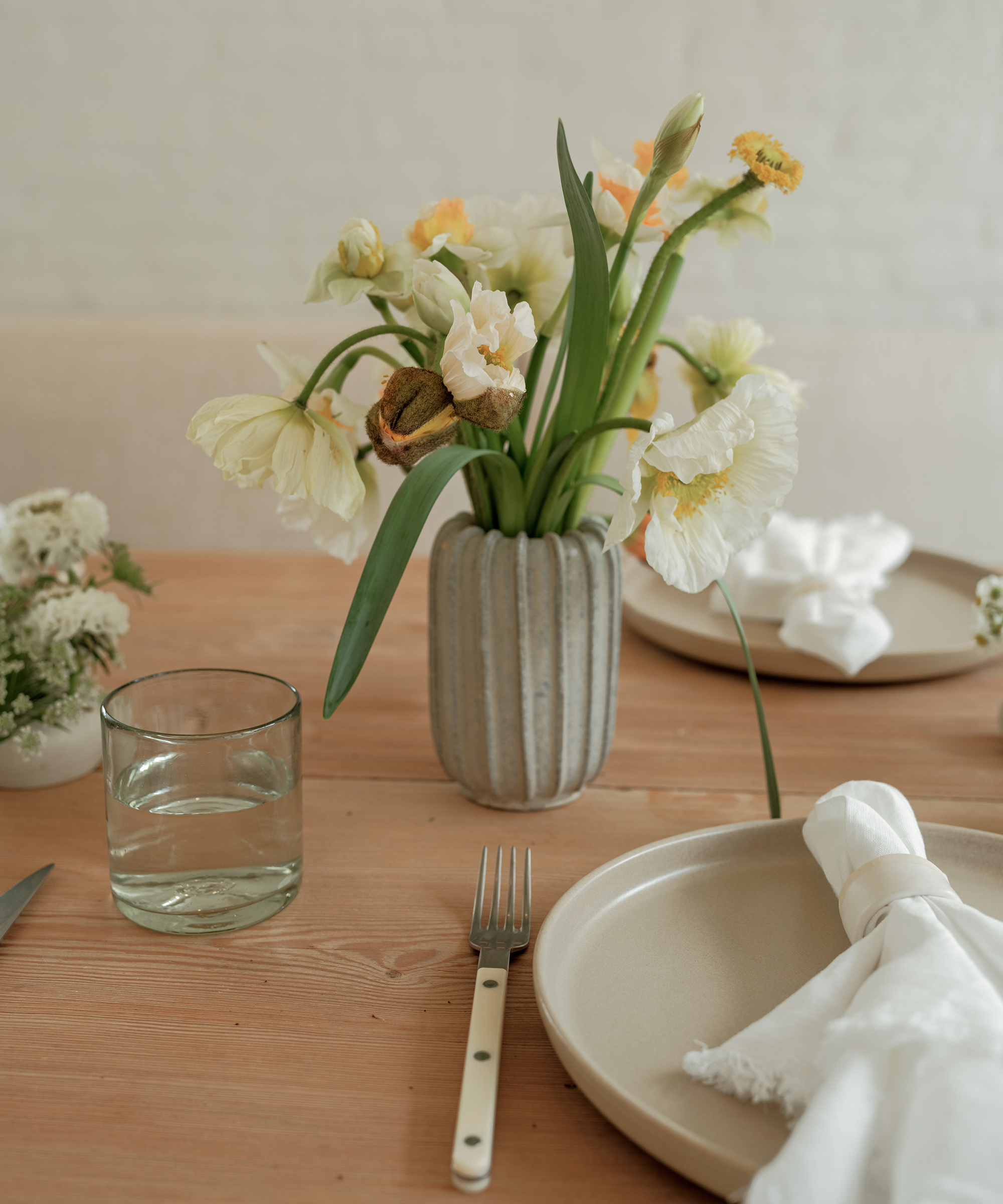 floral arrangement with drooping flowers in a grey ceramic vase on an oak dining table with two place settings