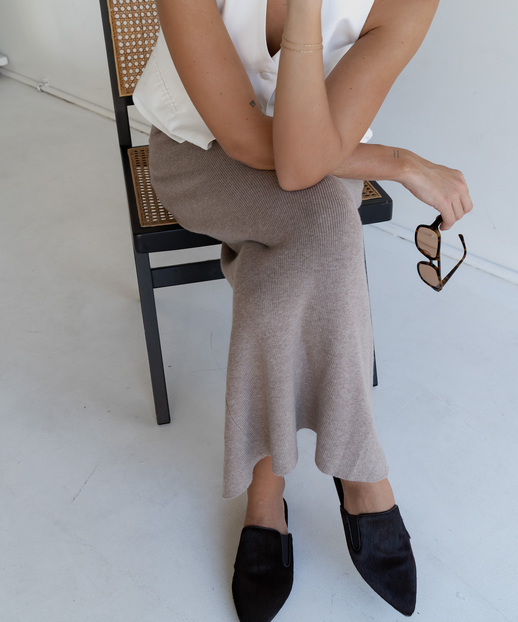 woman sitting with her legs crossed in an oatmeal sweater skirt and black mules