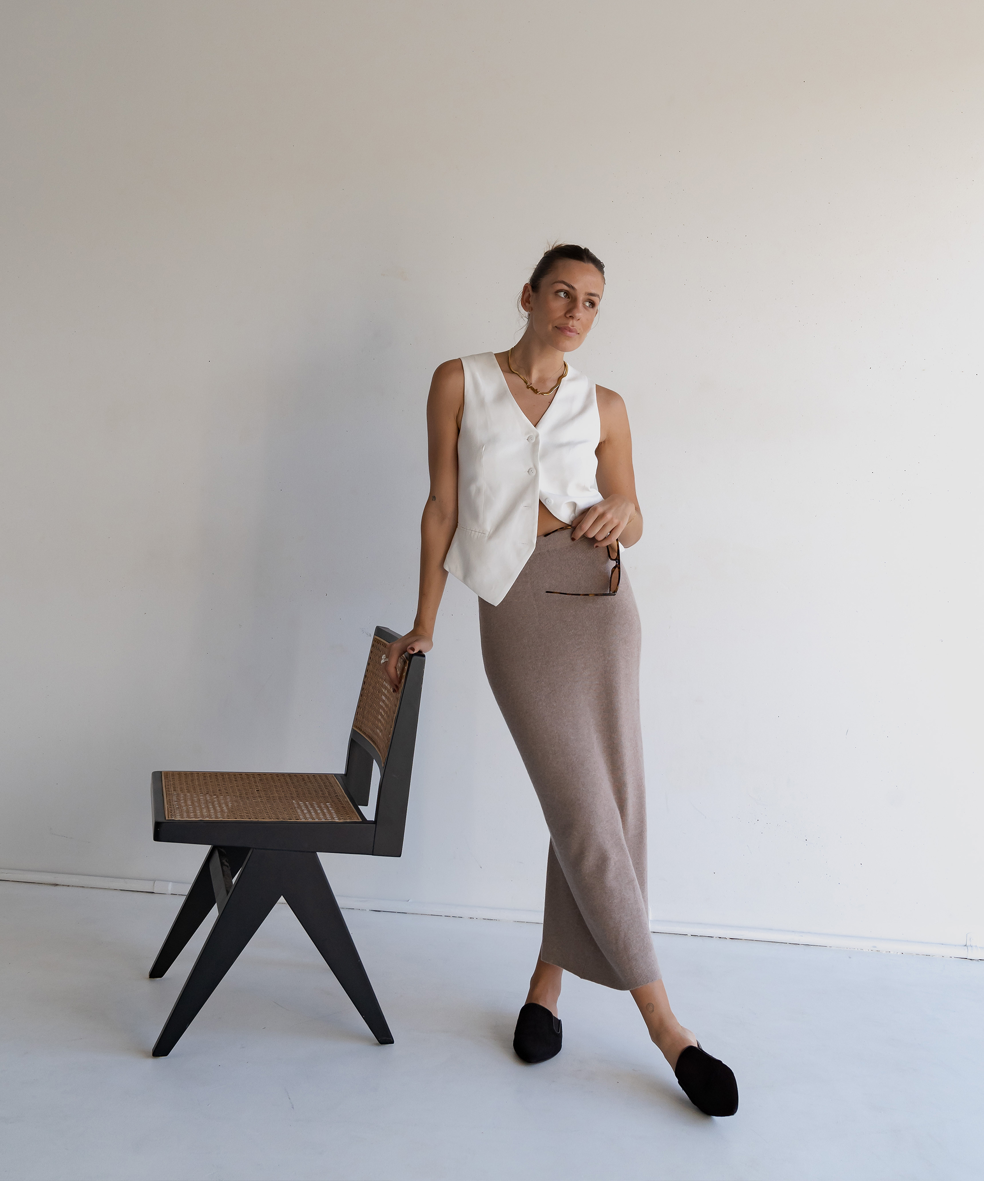 woman standing next to a cane chair in an oatmeal sweater skirt and white vest