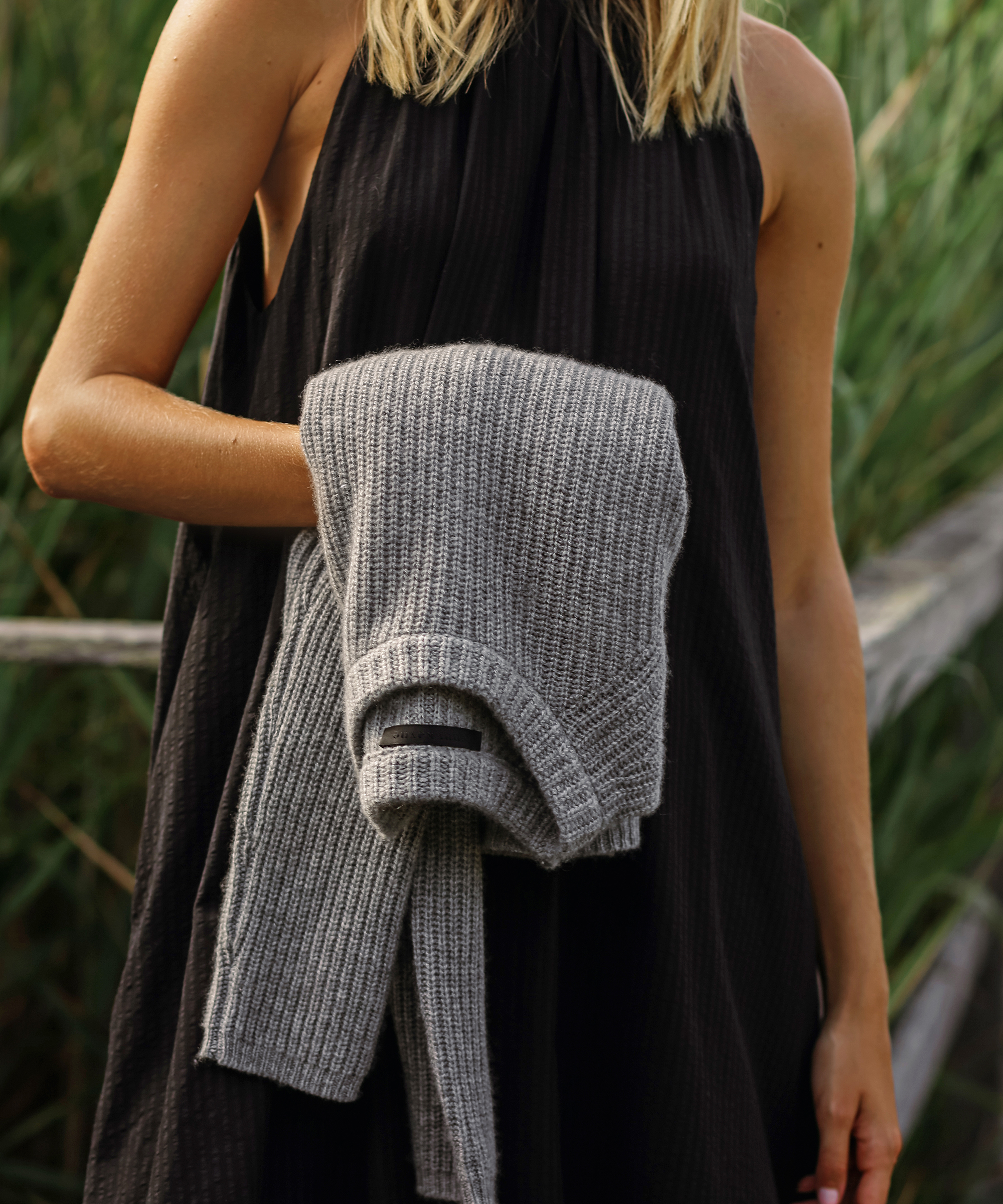 woman holding a grey cashmere sweater in a black dress