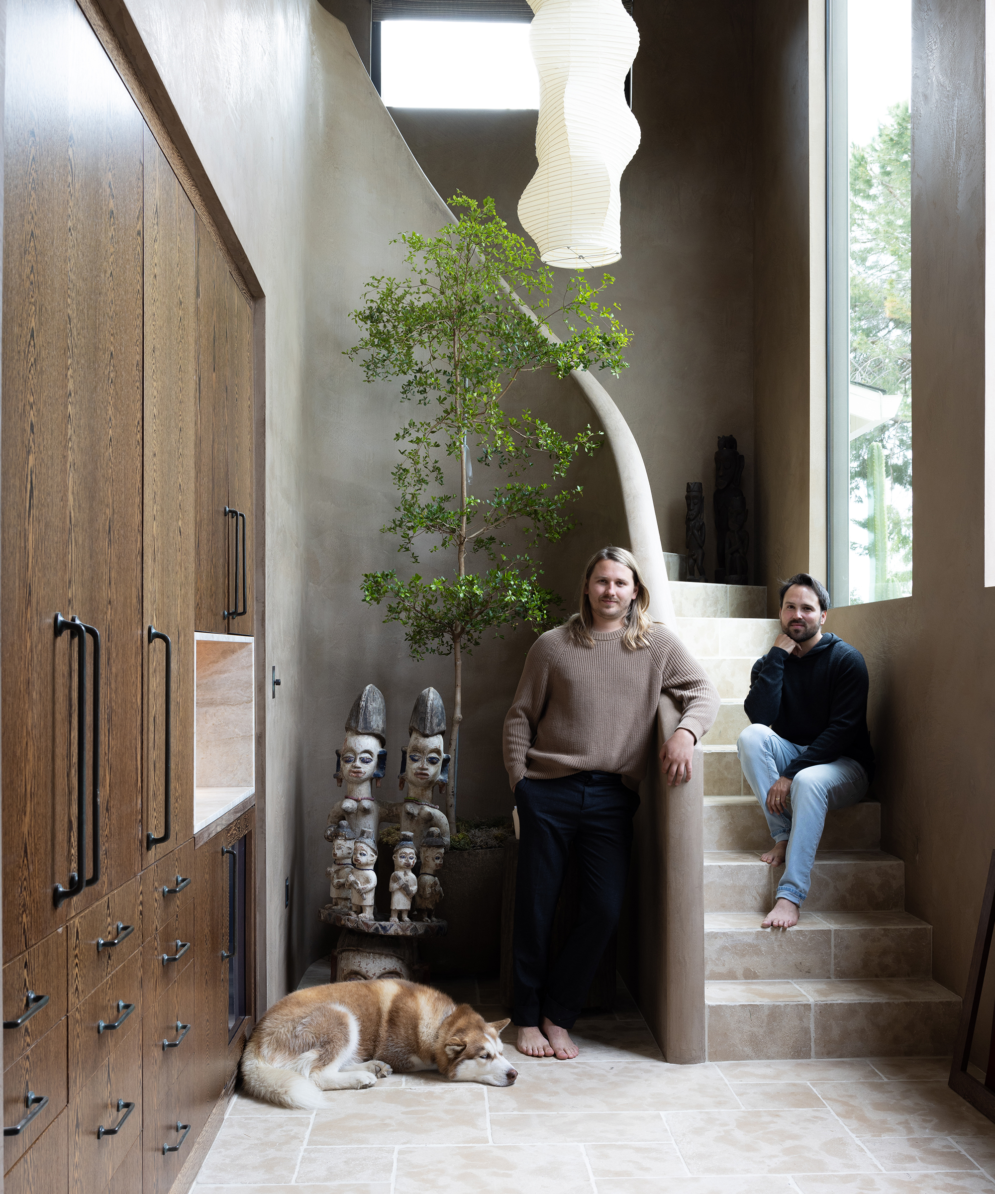stone stairwell with wooden built-ins lining the hall and two men standing in the stairwell with their dog next to a plant
