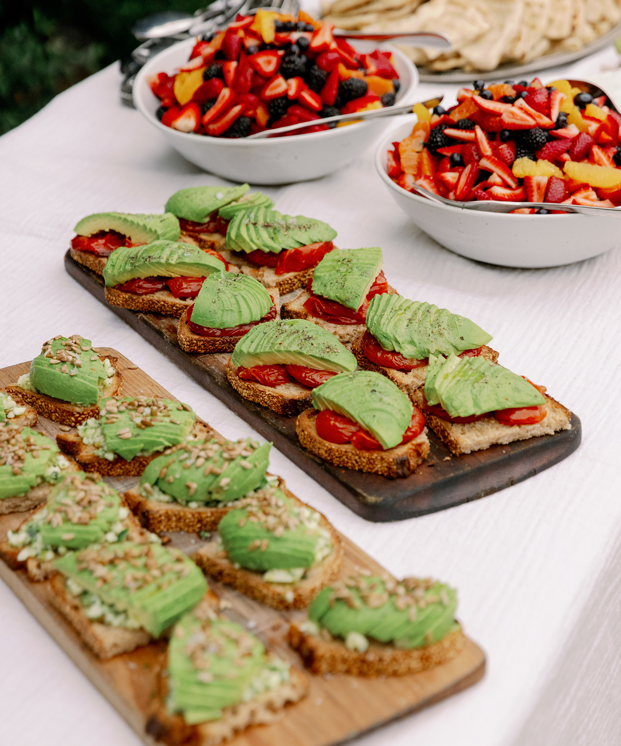 trays of food with avocado toast and berries on a white tablecloth
