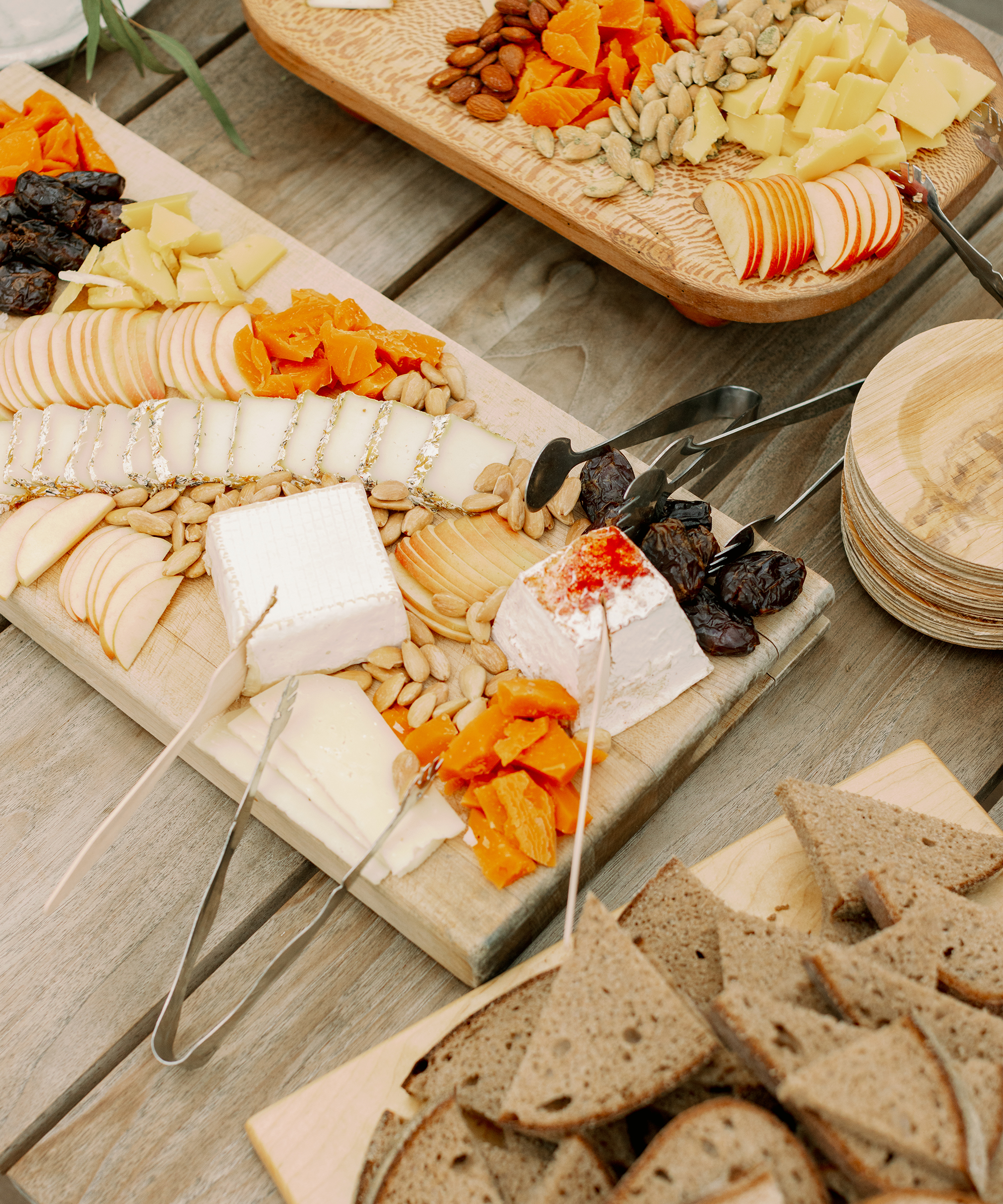 a wooden cheeseboard with a variety of chesses and crackers and serving utensils