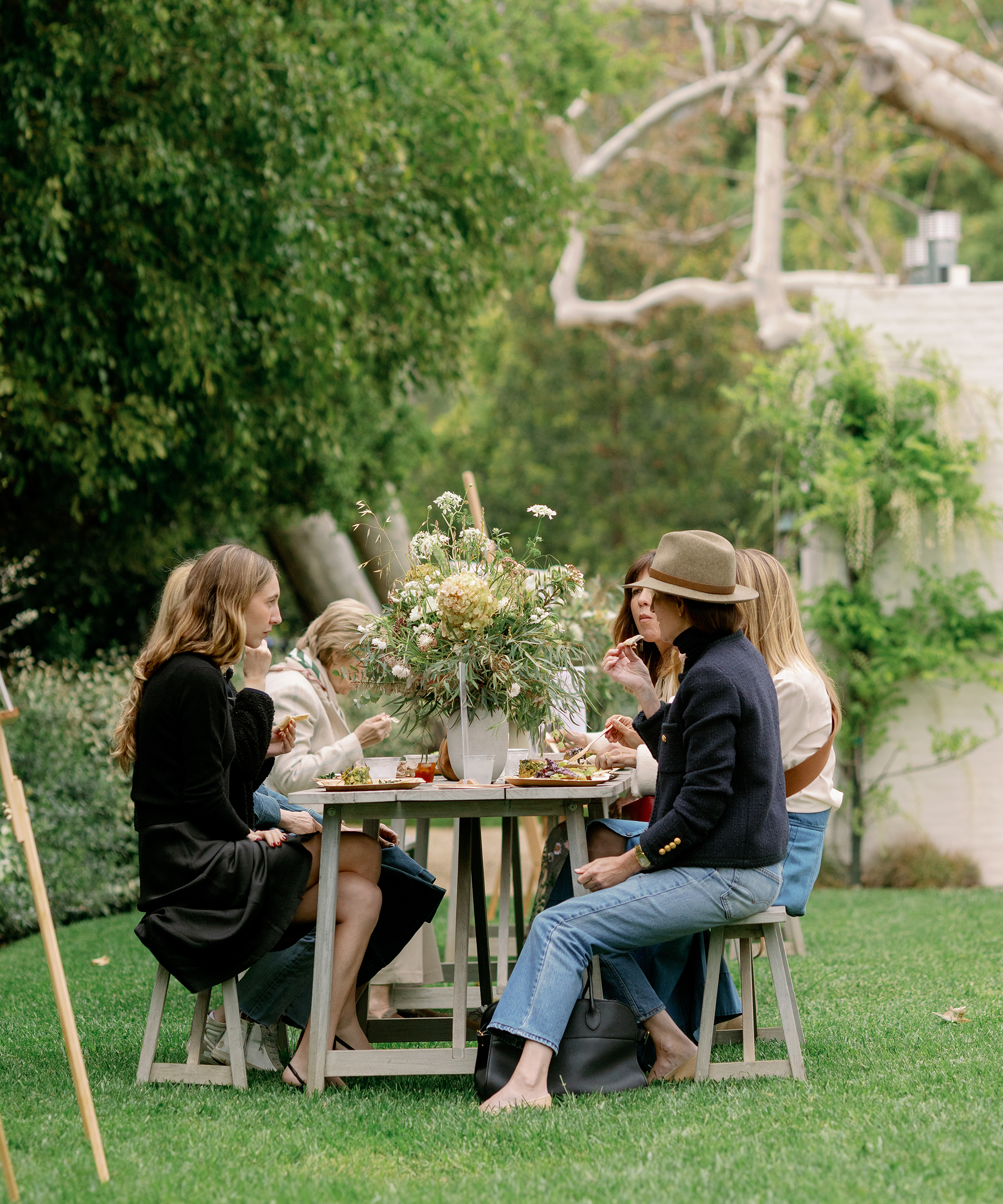 an outdoor dining table in the grass with women sitting and eating food