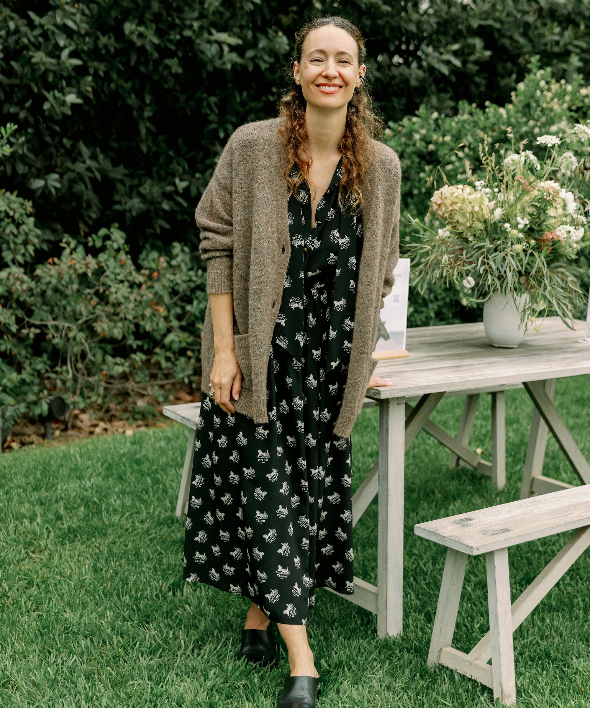 jenni kayne standing next to a table in a black patterned maxi dress and oatmeal cashmere cardigan