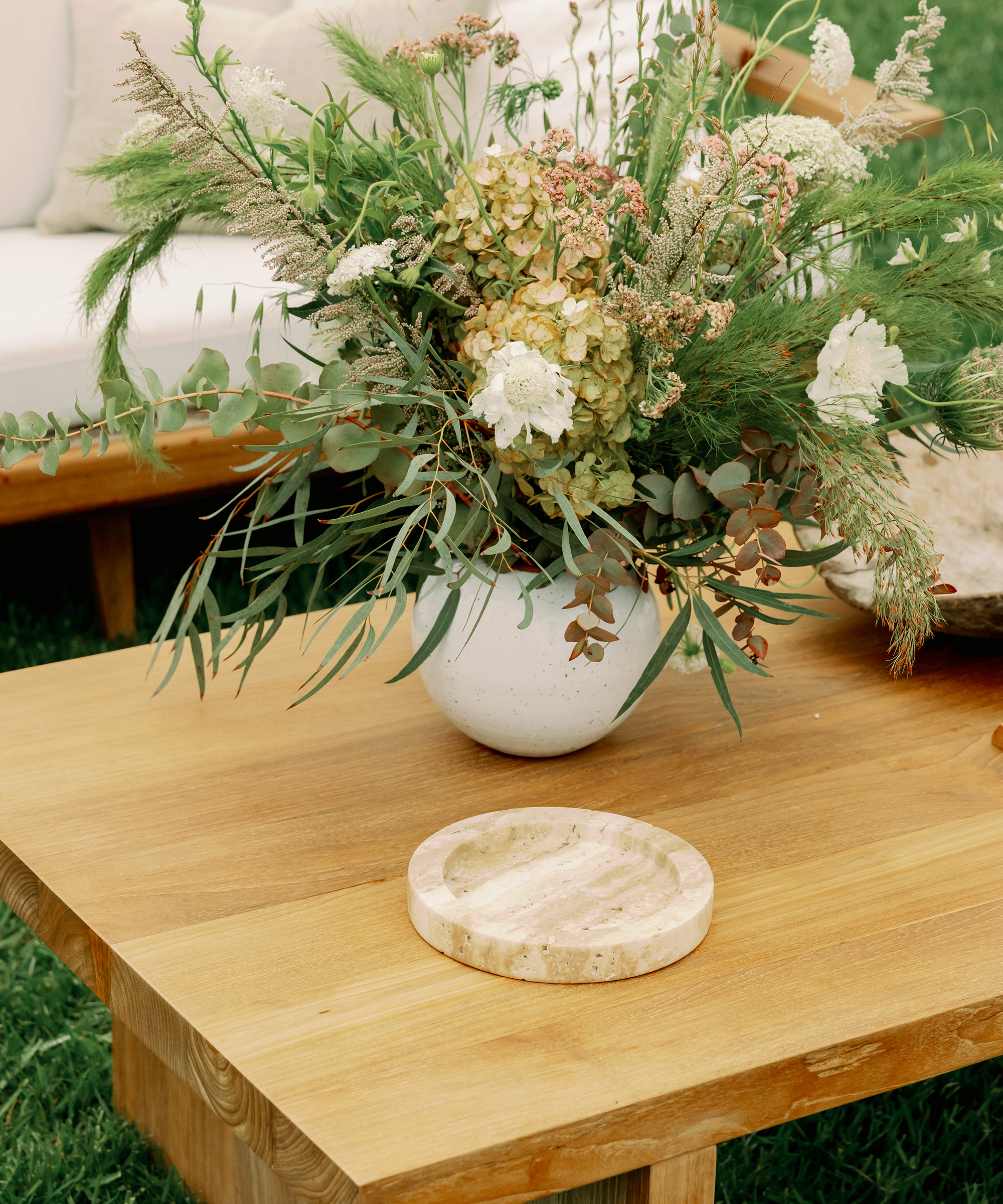 outdoor coffee table with a large vase of green and white flowers and a travertine decorative tray