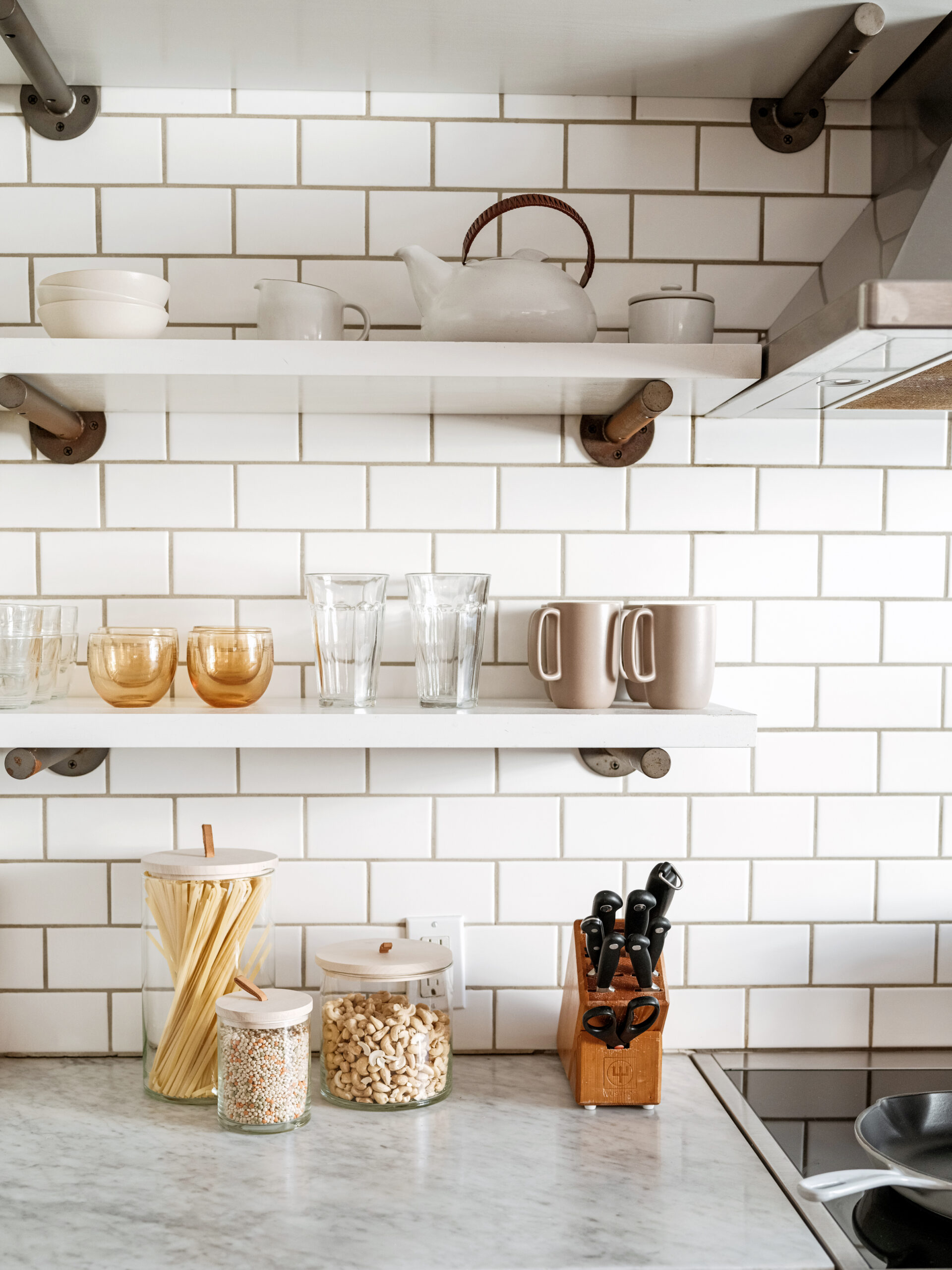 white tile backsplash in a kitchen with white marble counters and clear storage jars on the counter