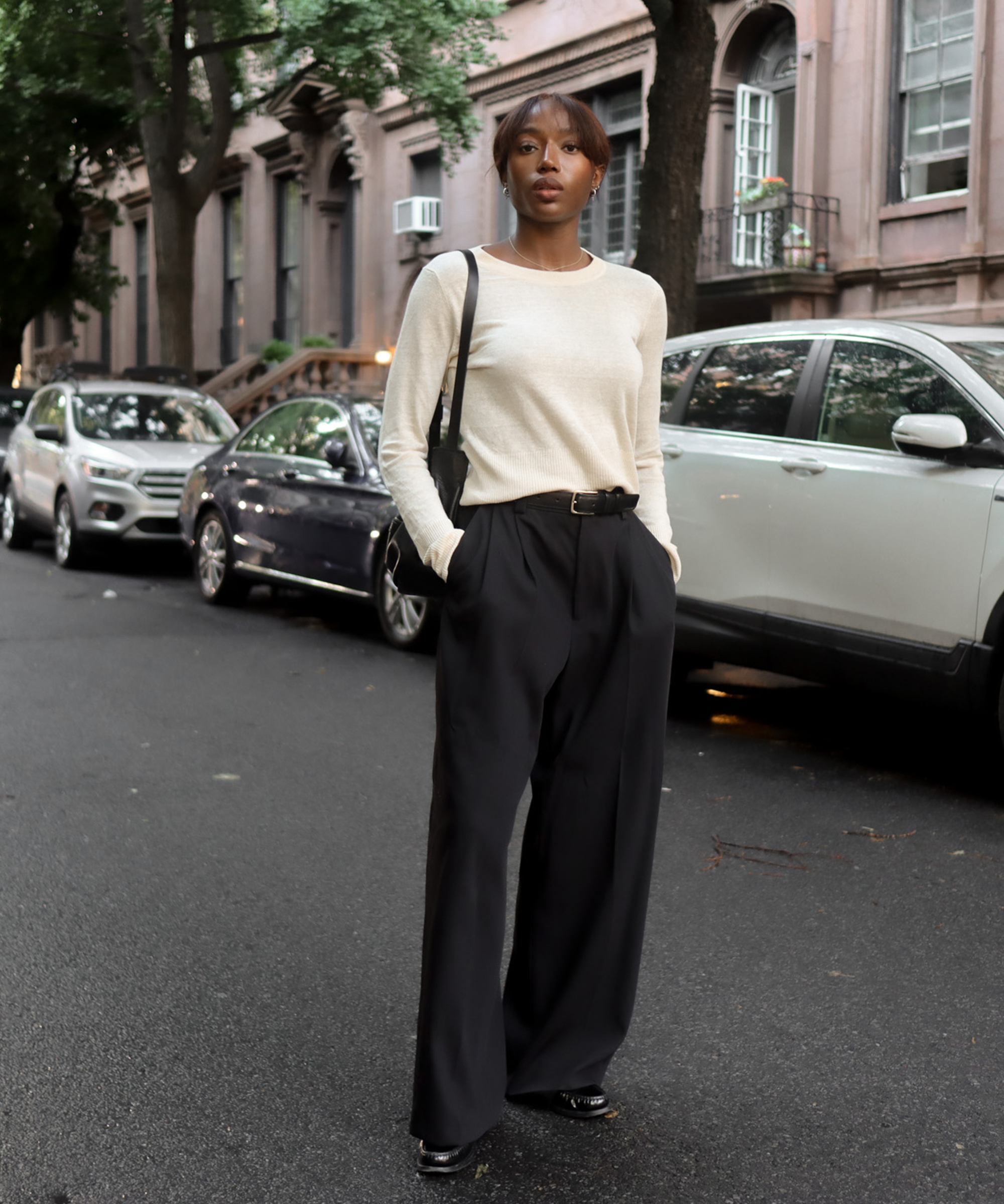 a woman standing in the streets of new york in a creme linen finley crewneck and black trousers and a black leather belt