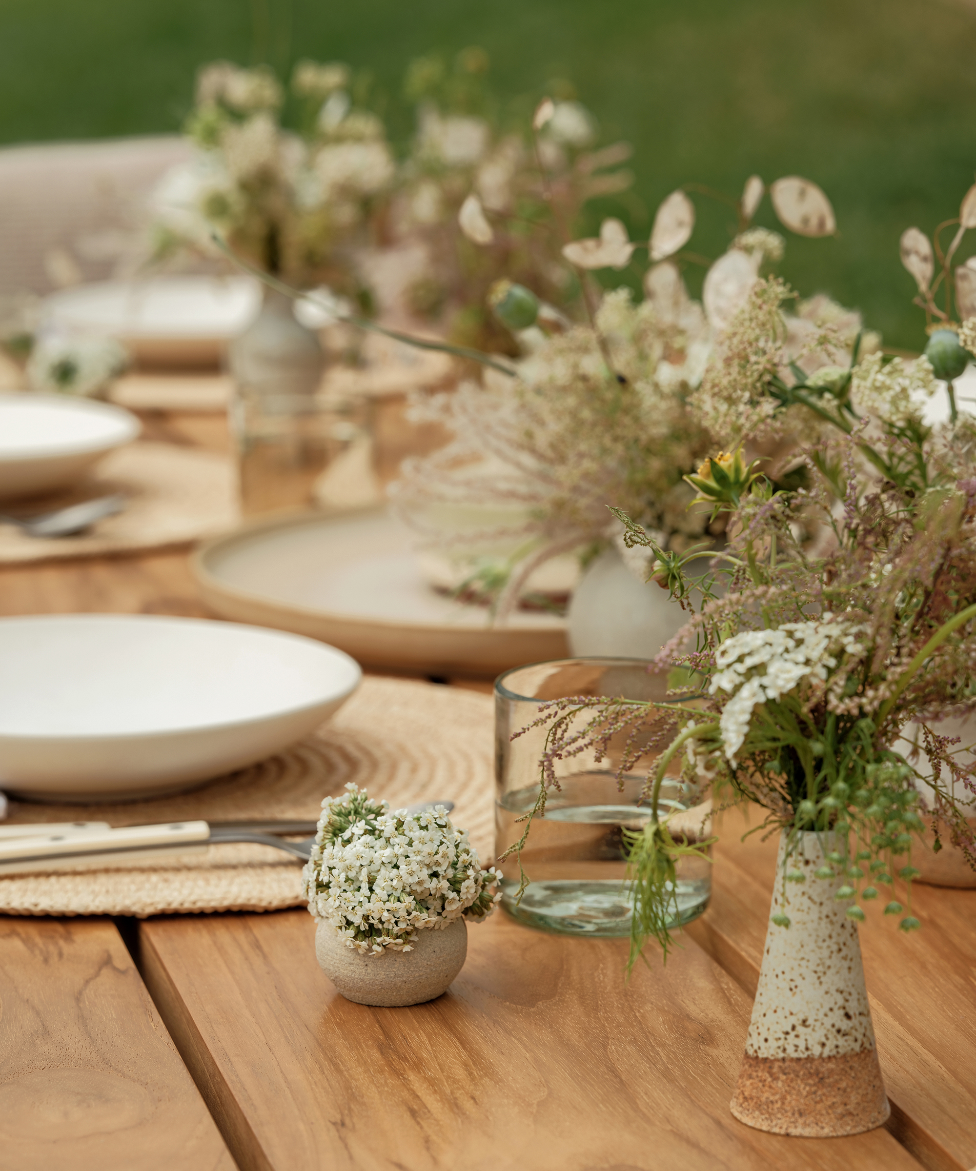 wood dining table with white and green florals in small ceramic vases