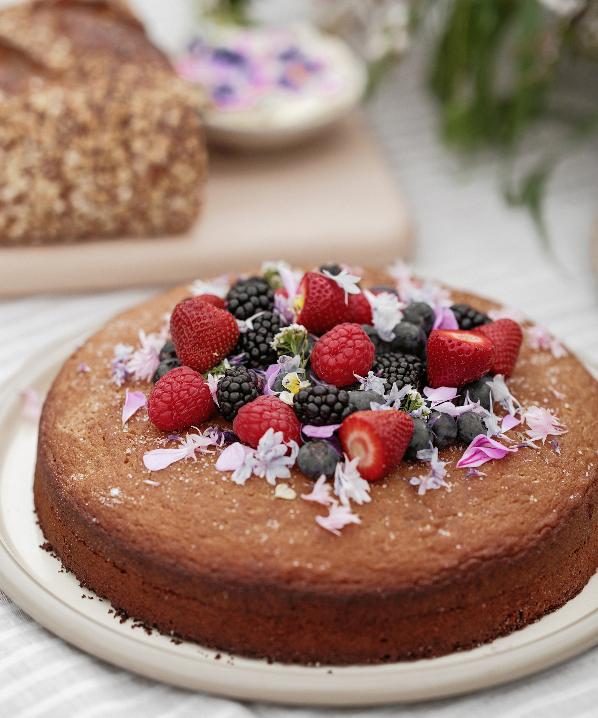 oilve oil cake topped with berries on a an outdoor serving plate on a striped linen tablecloth