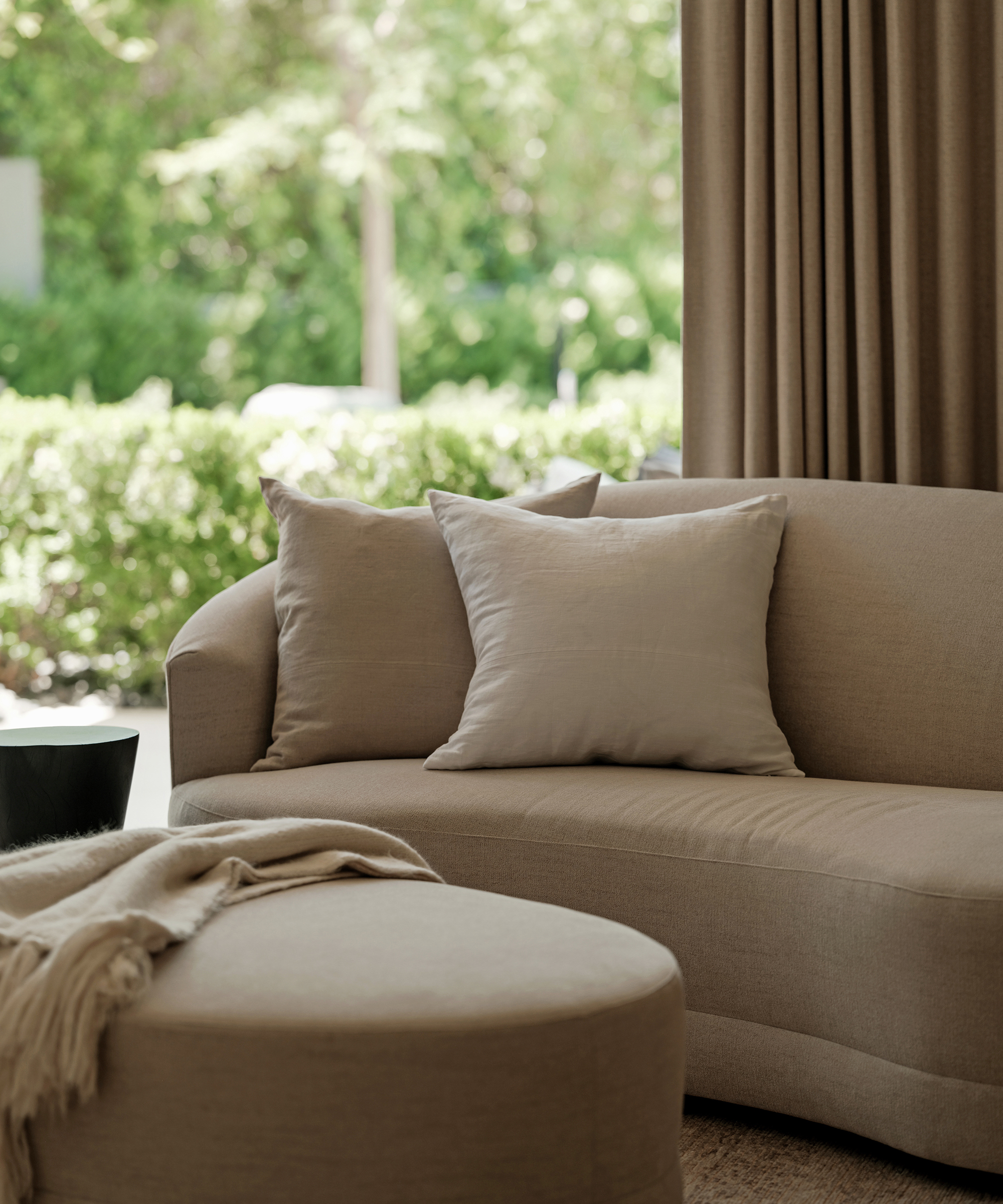 curved beige couch with two linen accent pillows in ivory and oatmeal in front of an open door