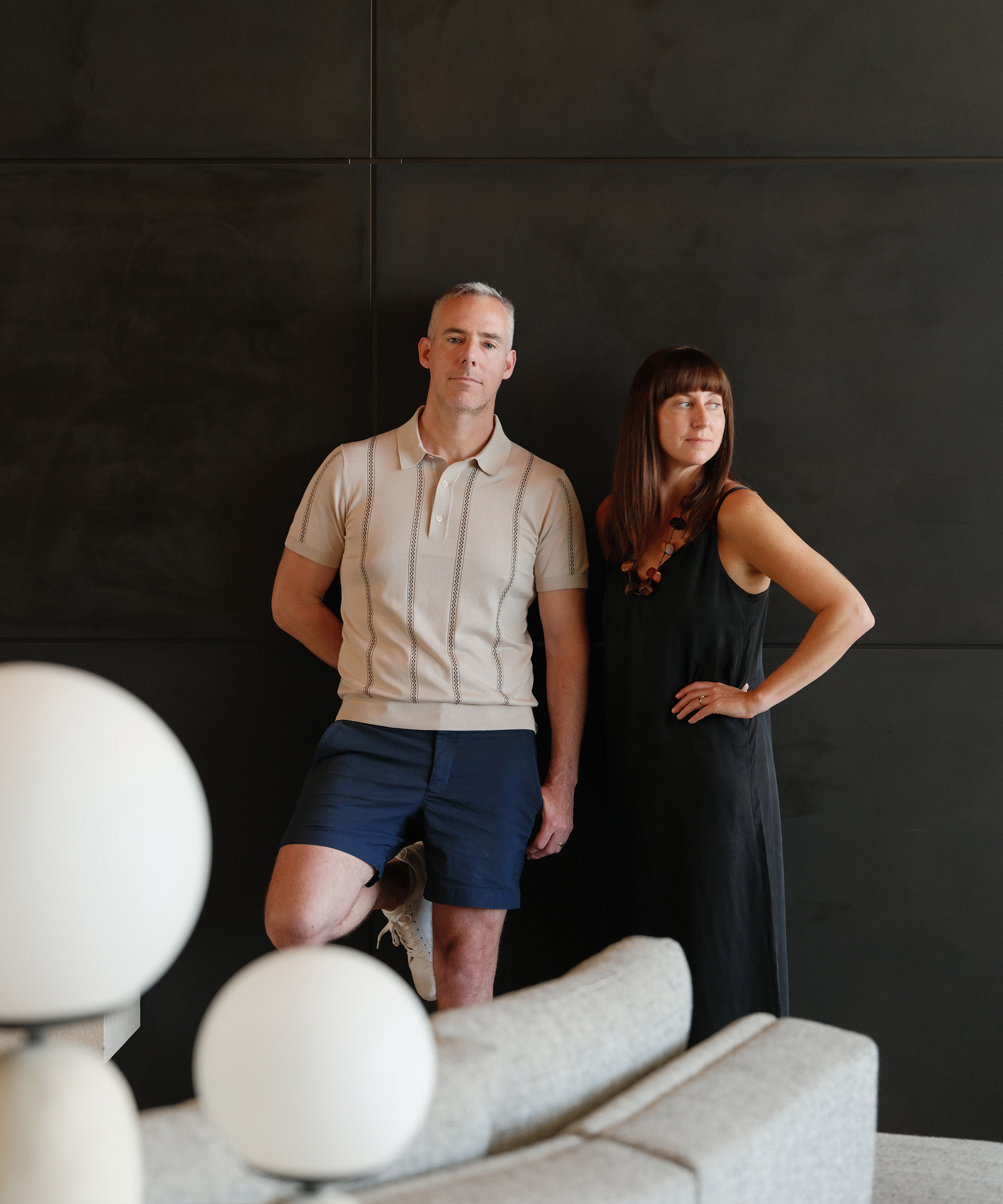 david and suzie lucas posing in front of a black accent wall in a living room