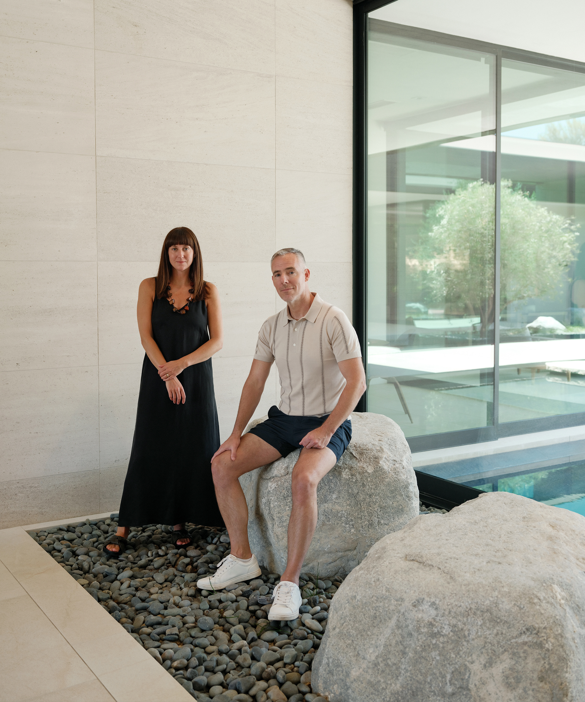 suzie in a black maxi dress and david lucas in a striped polo and chino shorts sitting on an indoor rock art installation