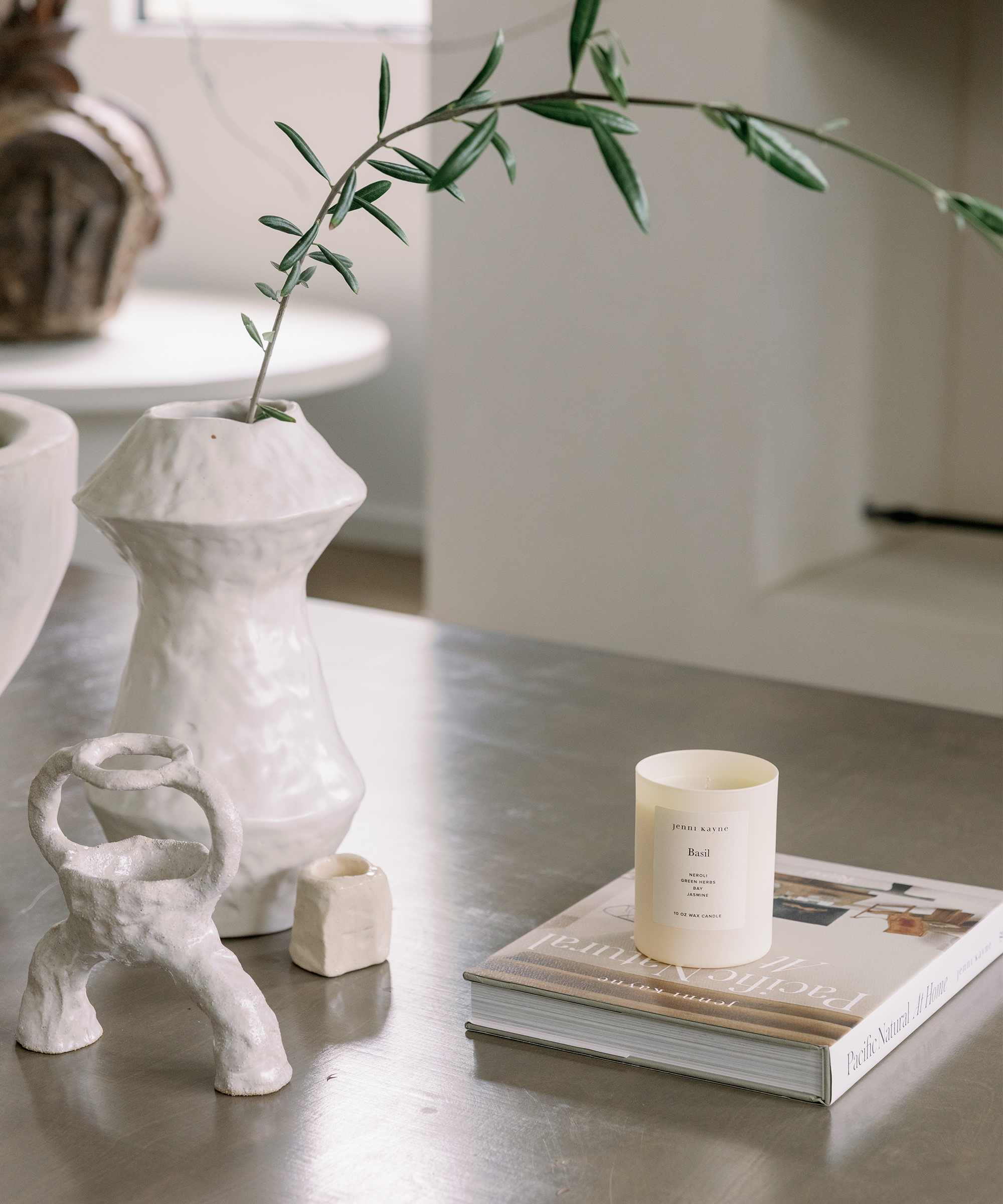 a stone coffee table with pacific natural at home coffee table book and a basil candle next to two white ceramic vases
