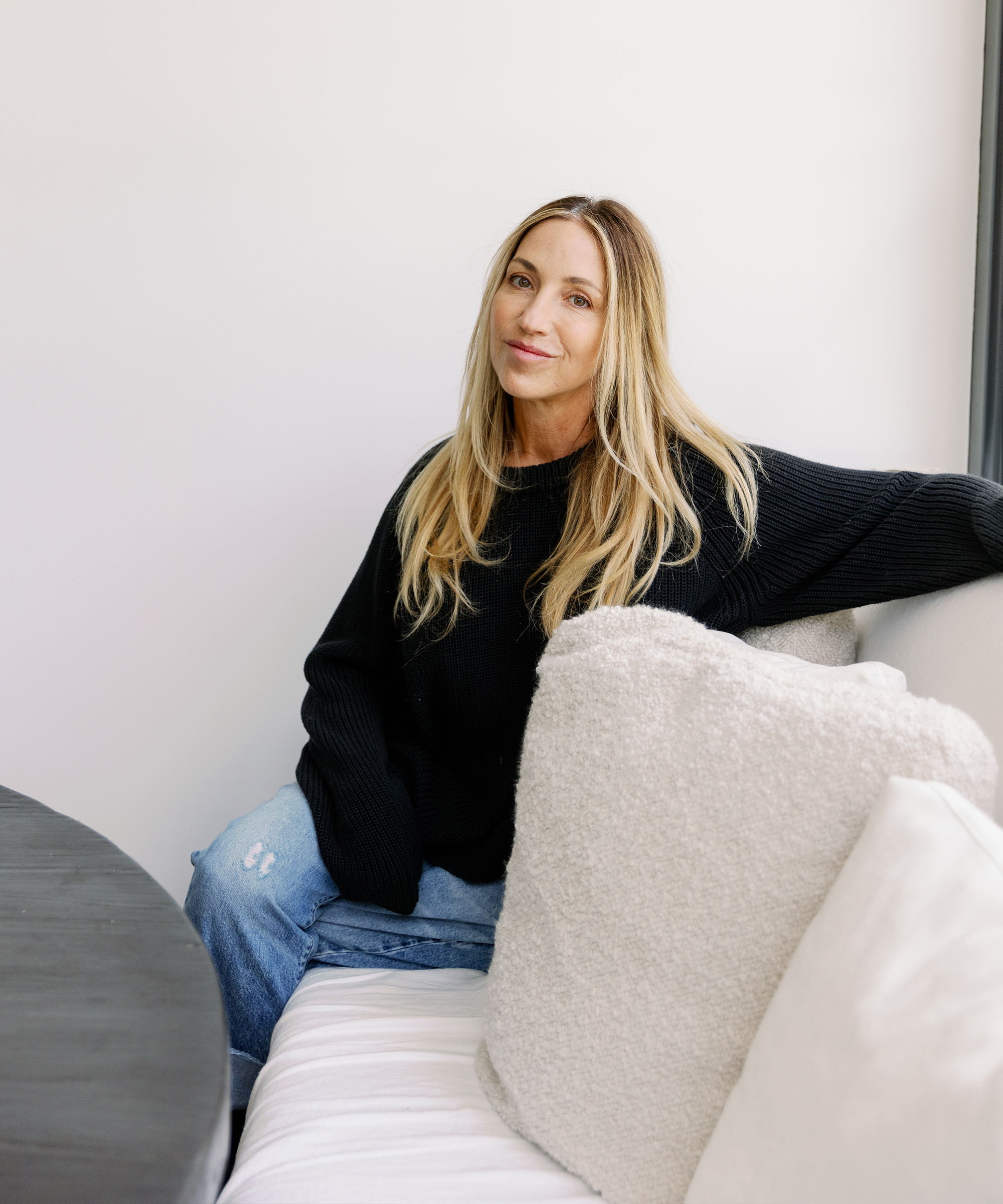 rachael goddard sitting on a white breakfast nook bench in a black cotton fisherman sweater and jeans