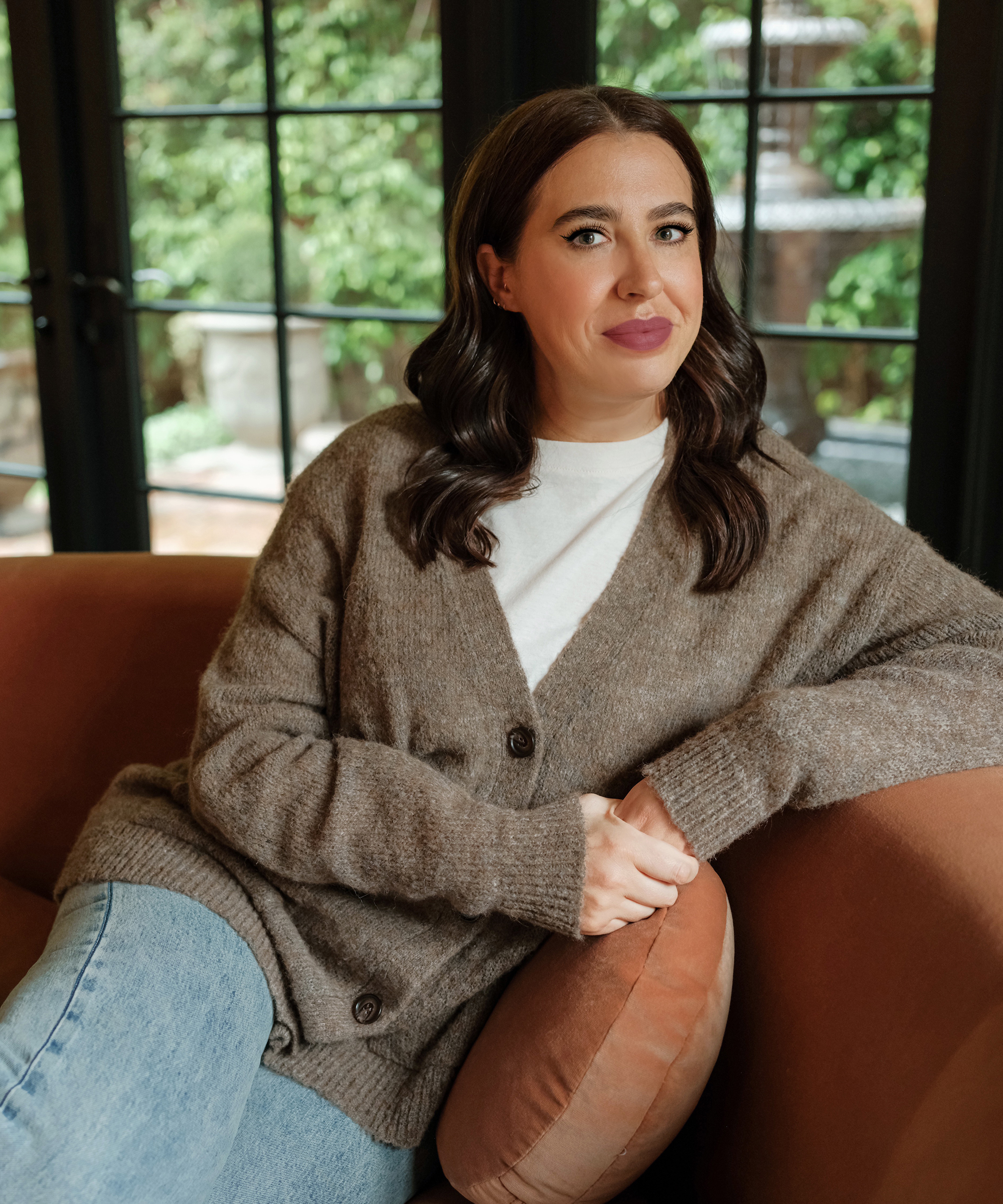 portrait of aliza in a taupe cardigan on a pink couch