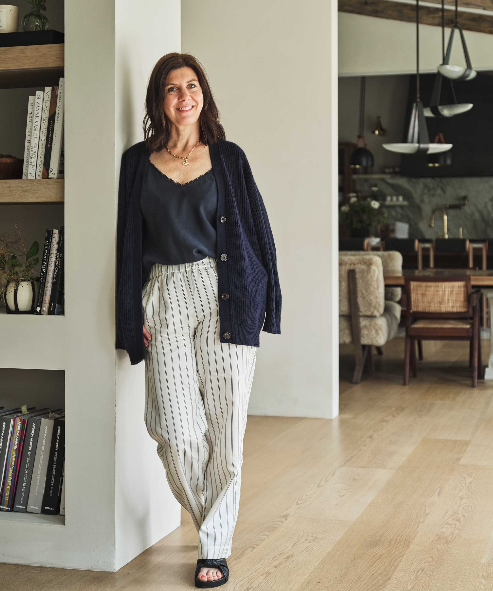 birgit klein leaning against a wall in white and navy striped pants and a navy cardigan sweater