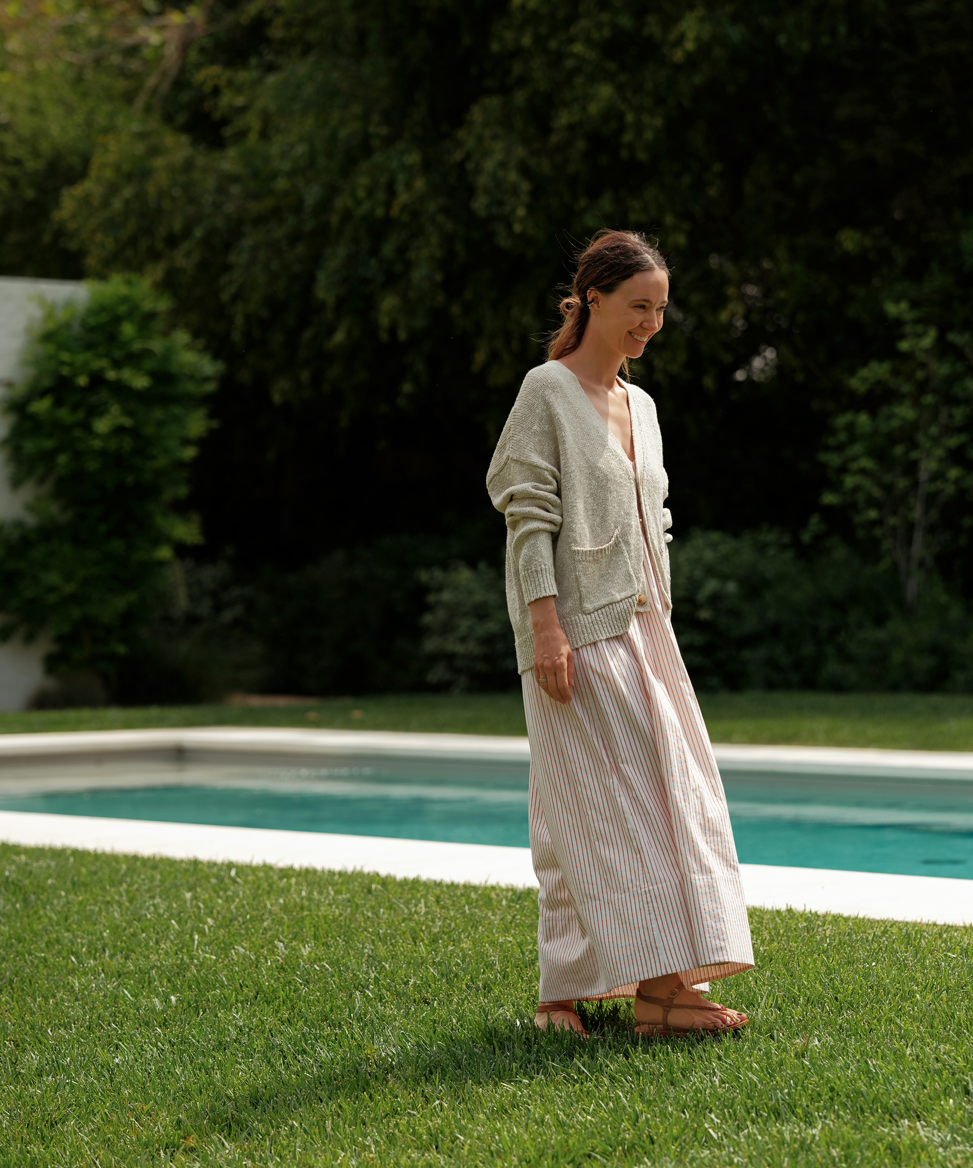 jenni kayne in a striped maxi dress with a cropped lightweight cardigan walking in the grass