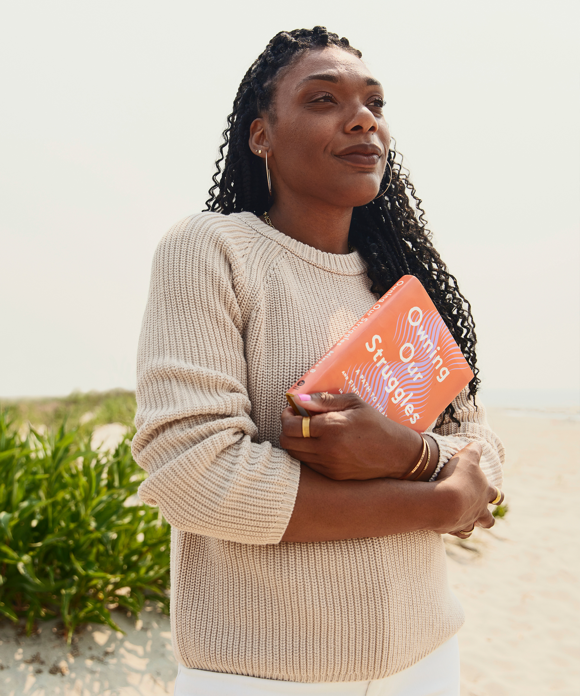 minaa holding her book owning our struggles in a camel fisherman sweater