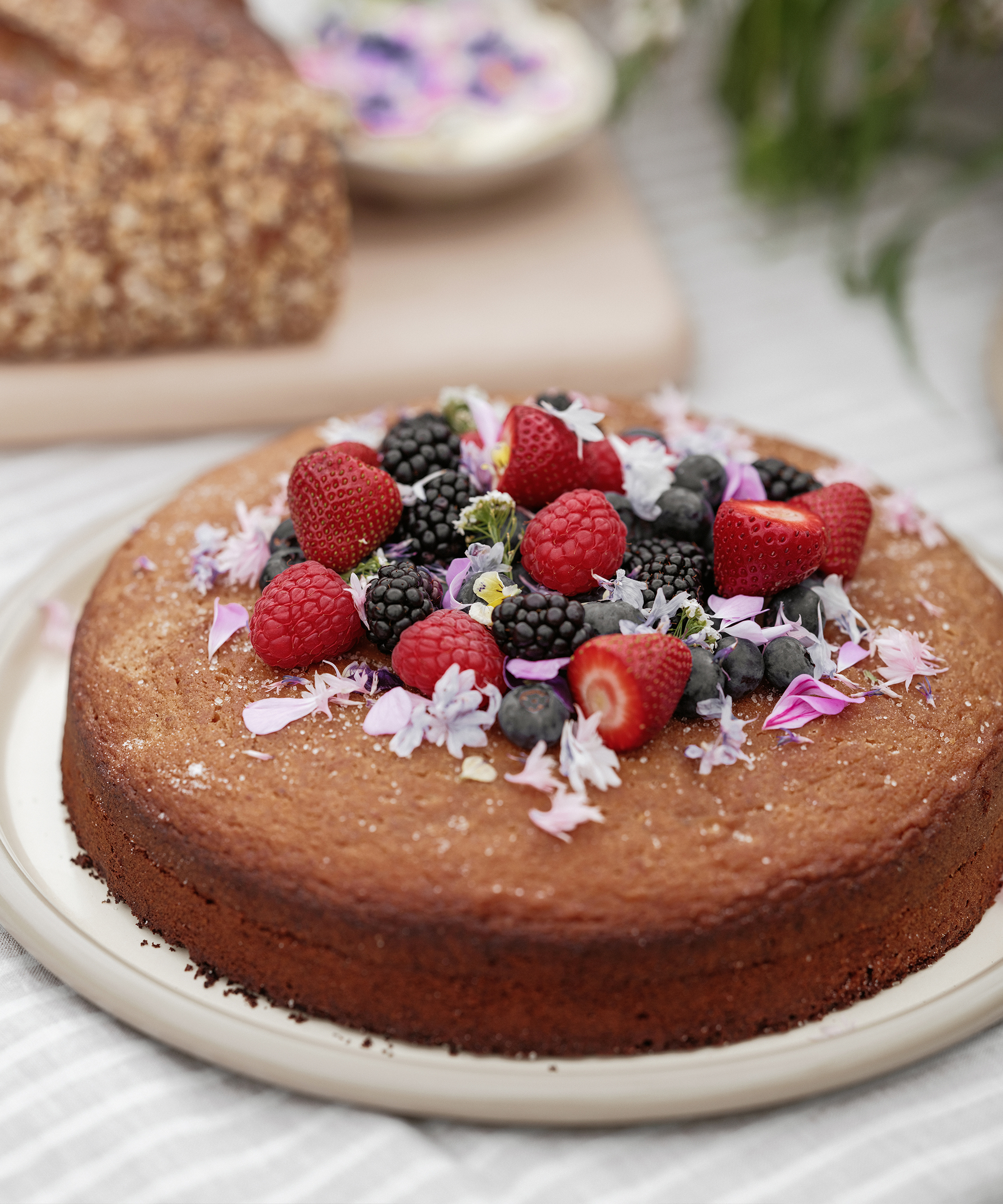 berry olive oil cake on a white picnic serving platter on a striped linen tablecloth