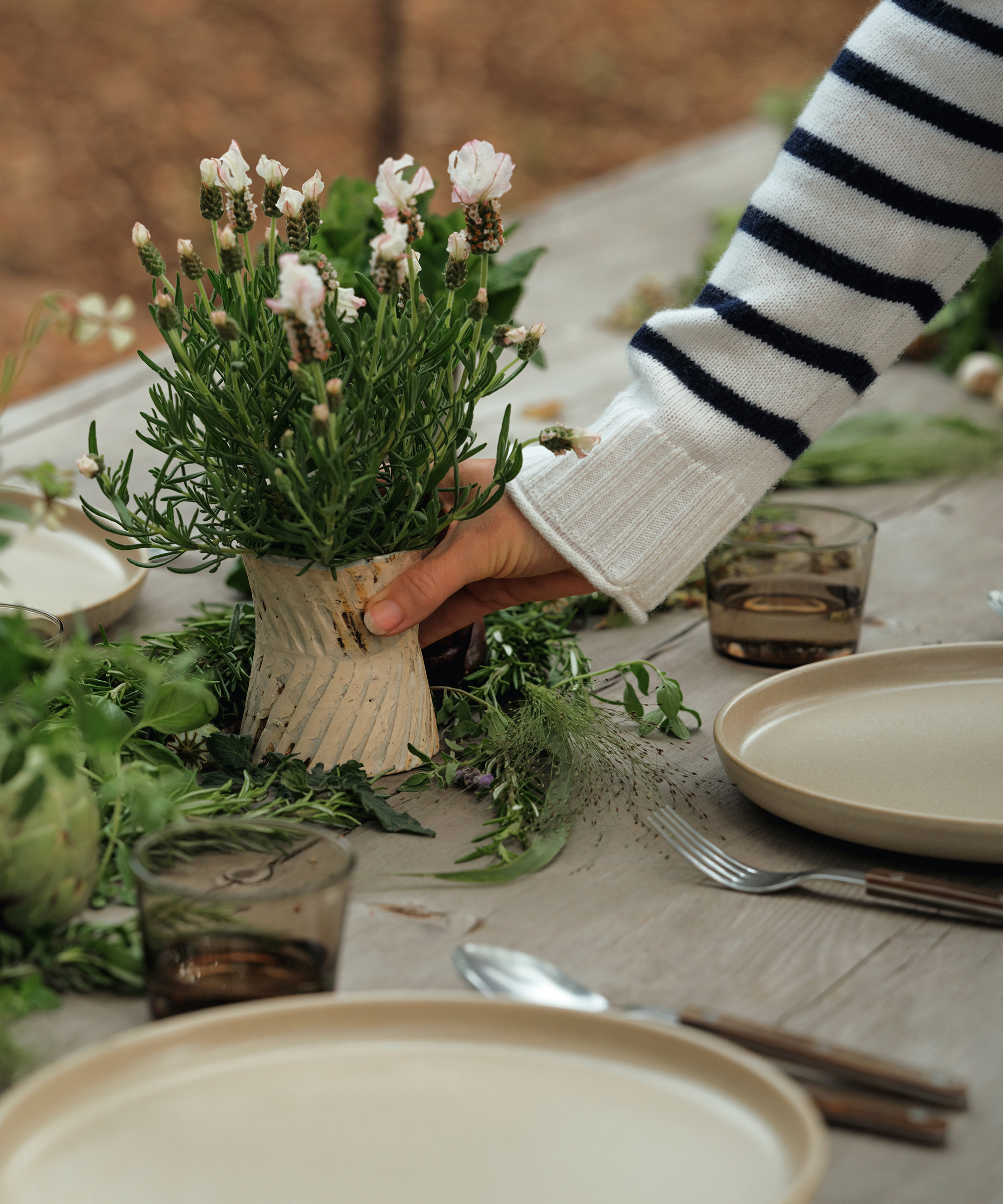jenni placing flowers in a small taupe vase on an outdoor dining table